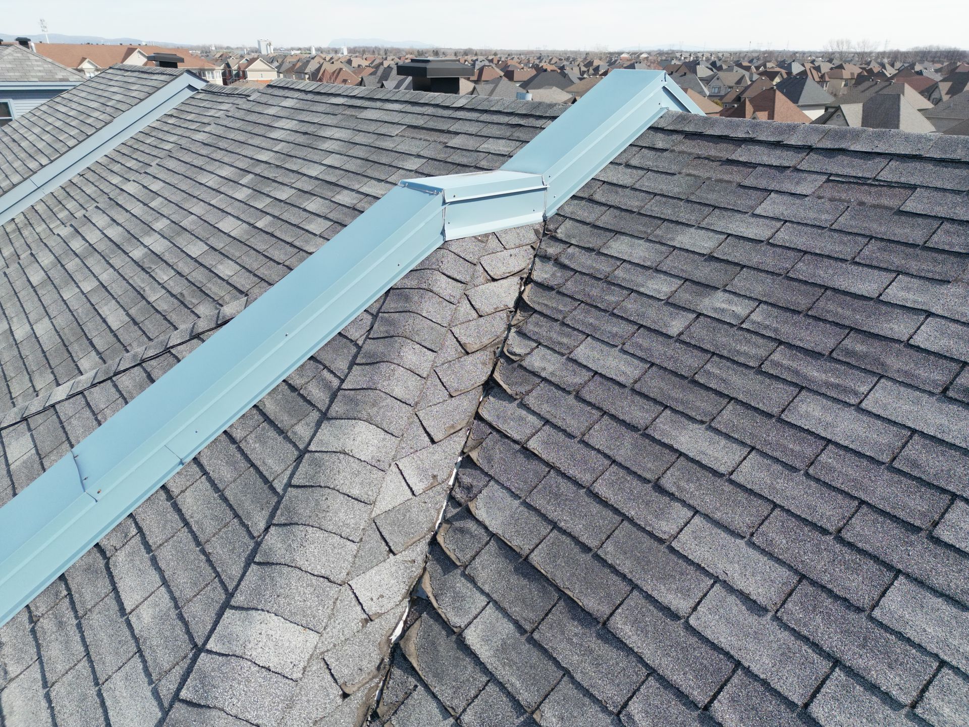 Roof valley with blue metal flashing between gray shingle rooftops