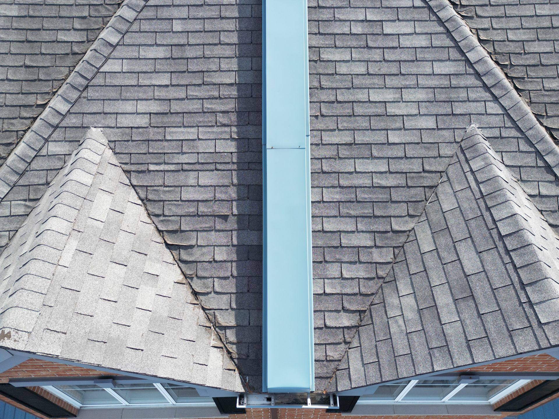 Roof with gray shingles and a central blue vent or chimney pipe, viewed from above.