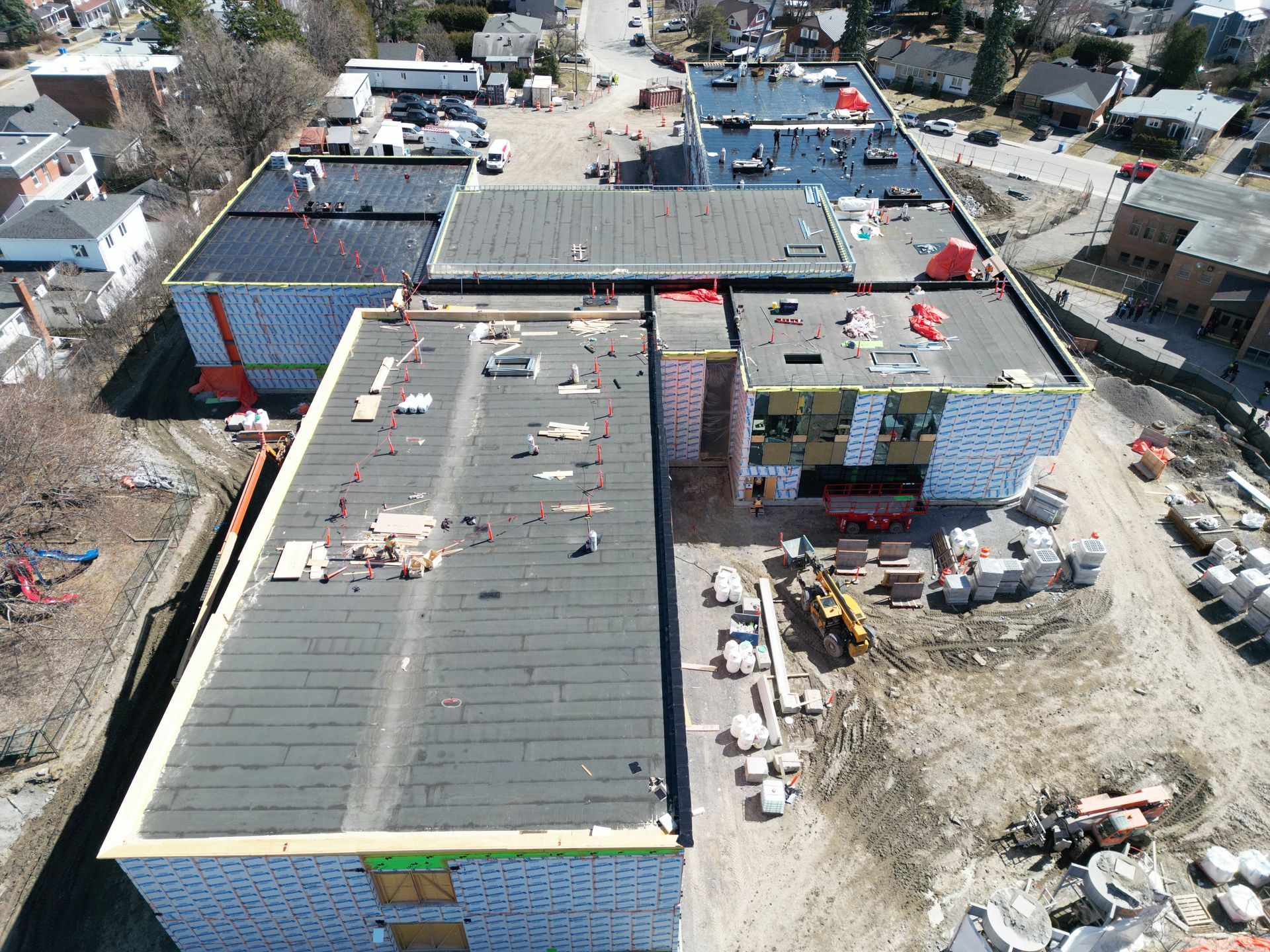 Aerial view of a construction site with multiple flat-roofed buildings and scattered building materials.