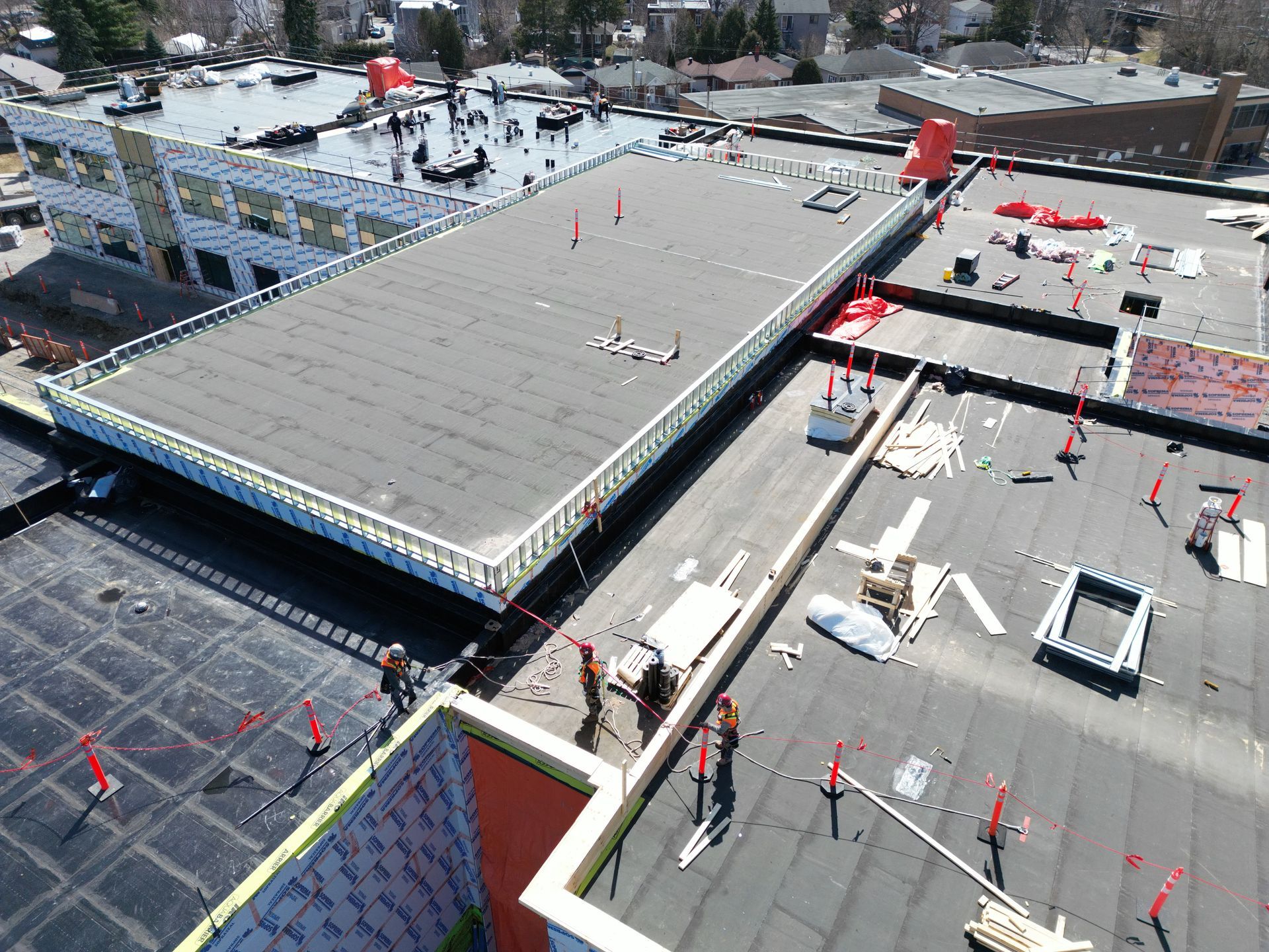 Aerial view of a rooftop construction site with workers, equipment, and snow-covered surroundings.