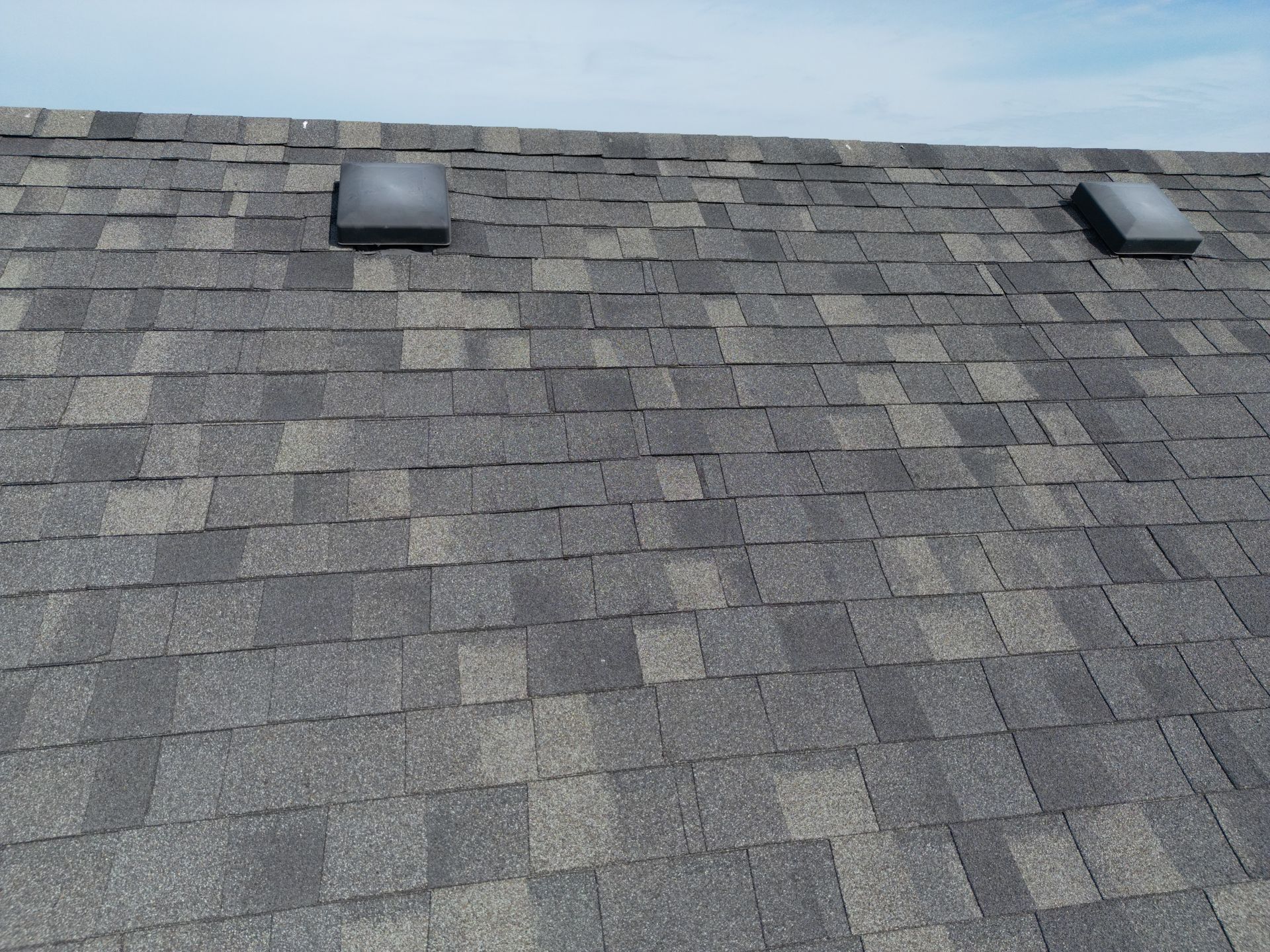 Gray shingled roof with two black roof vents under a blue sky