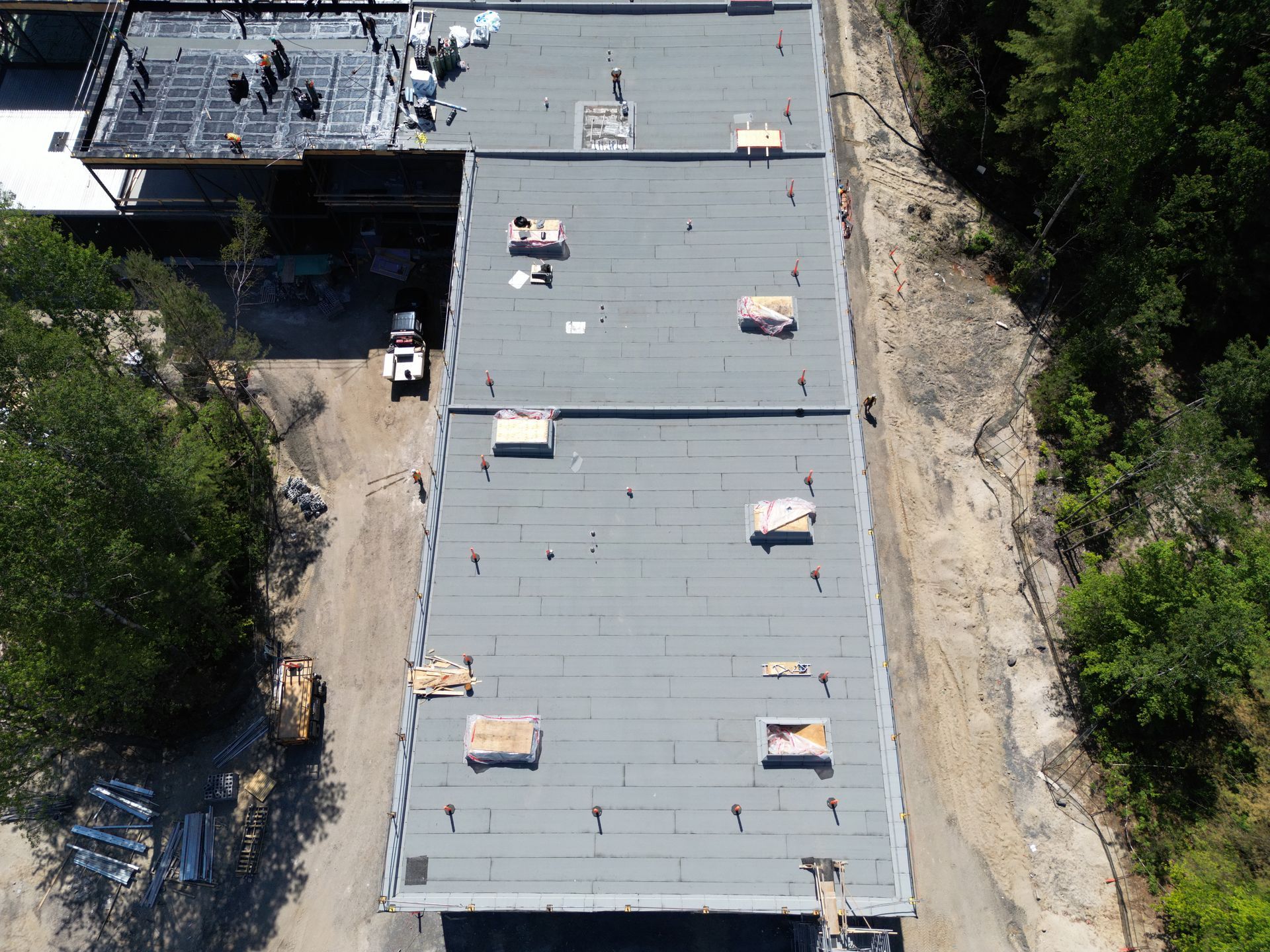 Aerial view of a flat-roofed building beside trees and a dirt path.