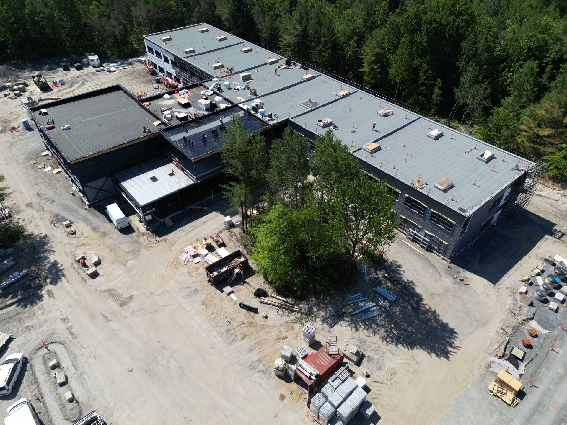 Aerial view of a large industrial building and construction yard surrounded by trees and dirt roads