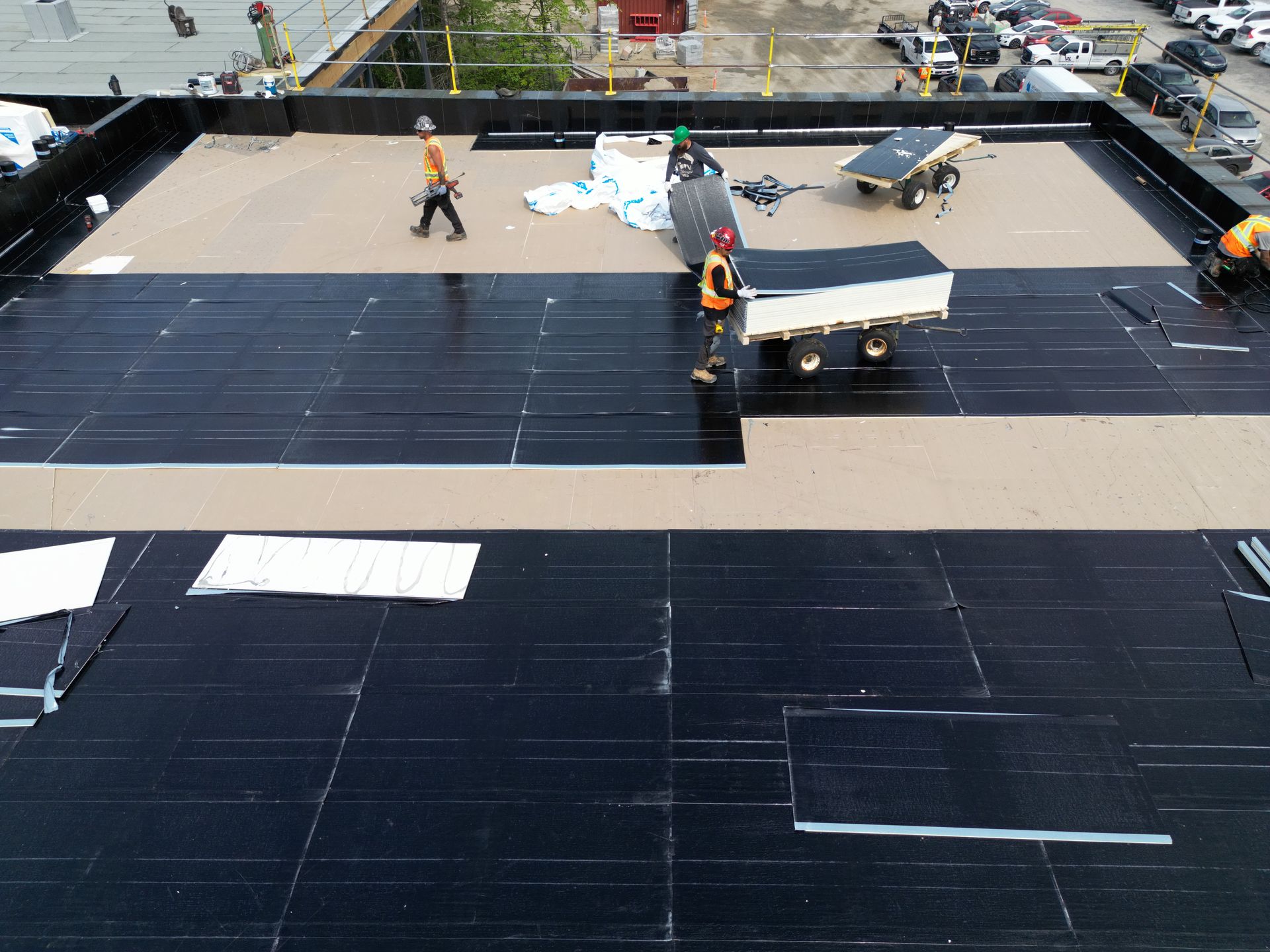 Workers installing dark roofing panels on a flat rooftop at a construction site