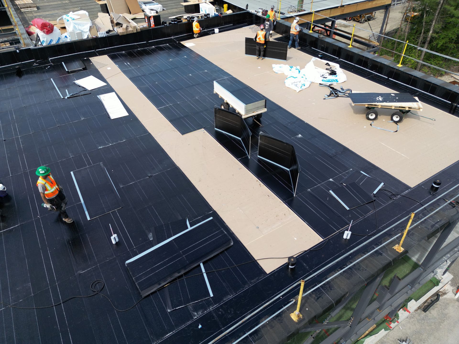 Construction site roof with workers installing large black panels and materials on a beige surface