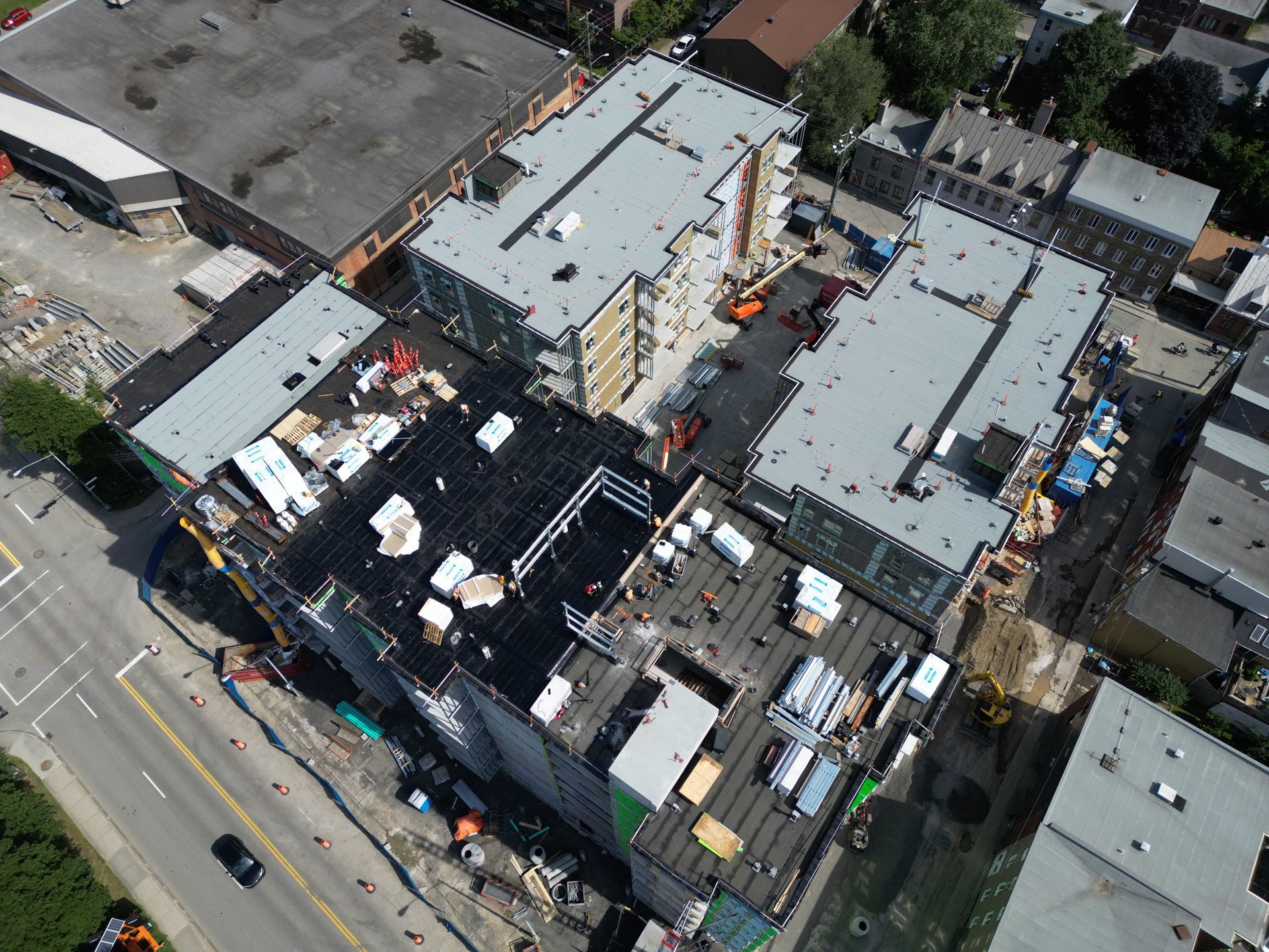 Aerial view of a multi-building construction site beside a road, with cranes and rooftop equipment.