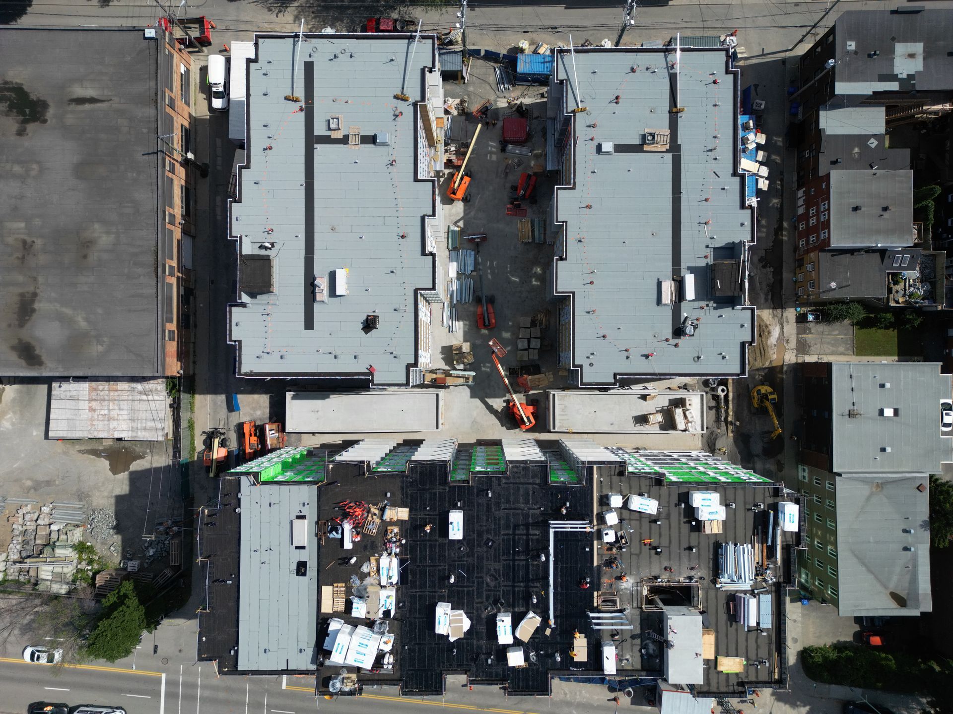 Aerial view of a building roof under construction, with workers, equipment, and materials visible.