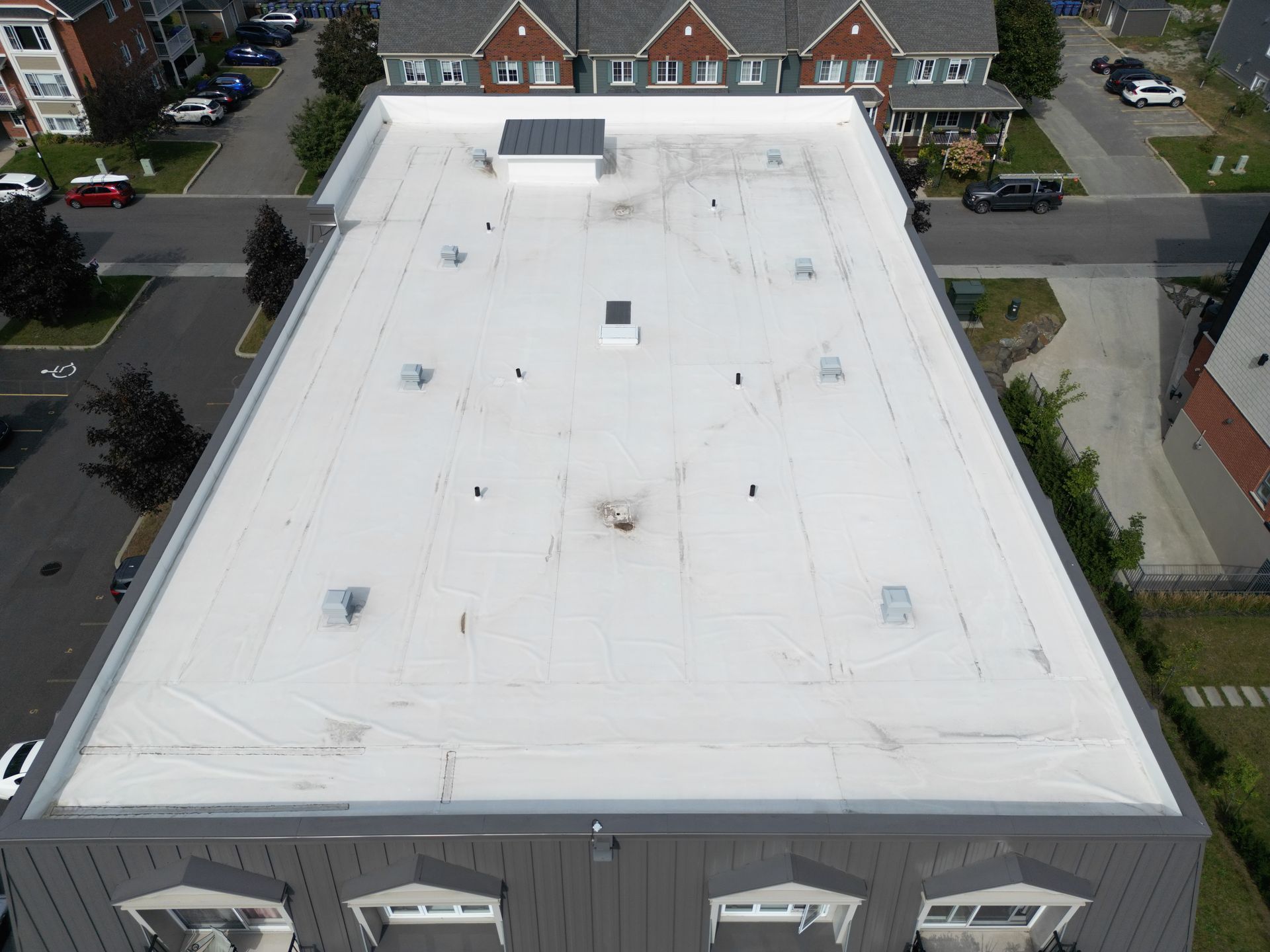 Aerial view of a flat white roof on a building in a residential neighborhood.