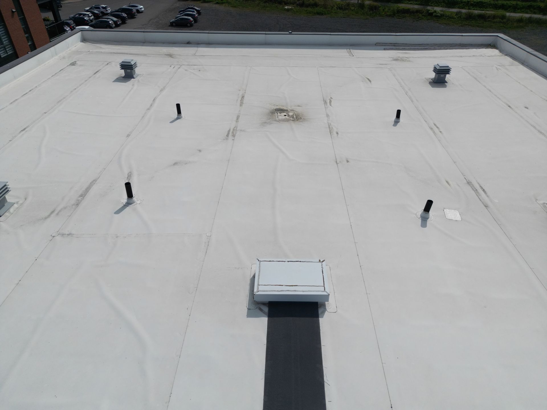Flat white rooftop with vents and a central HVAC unit, viewed from above