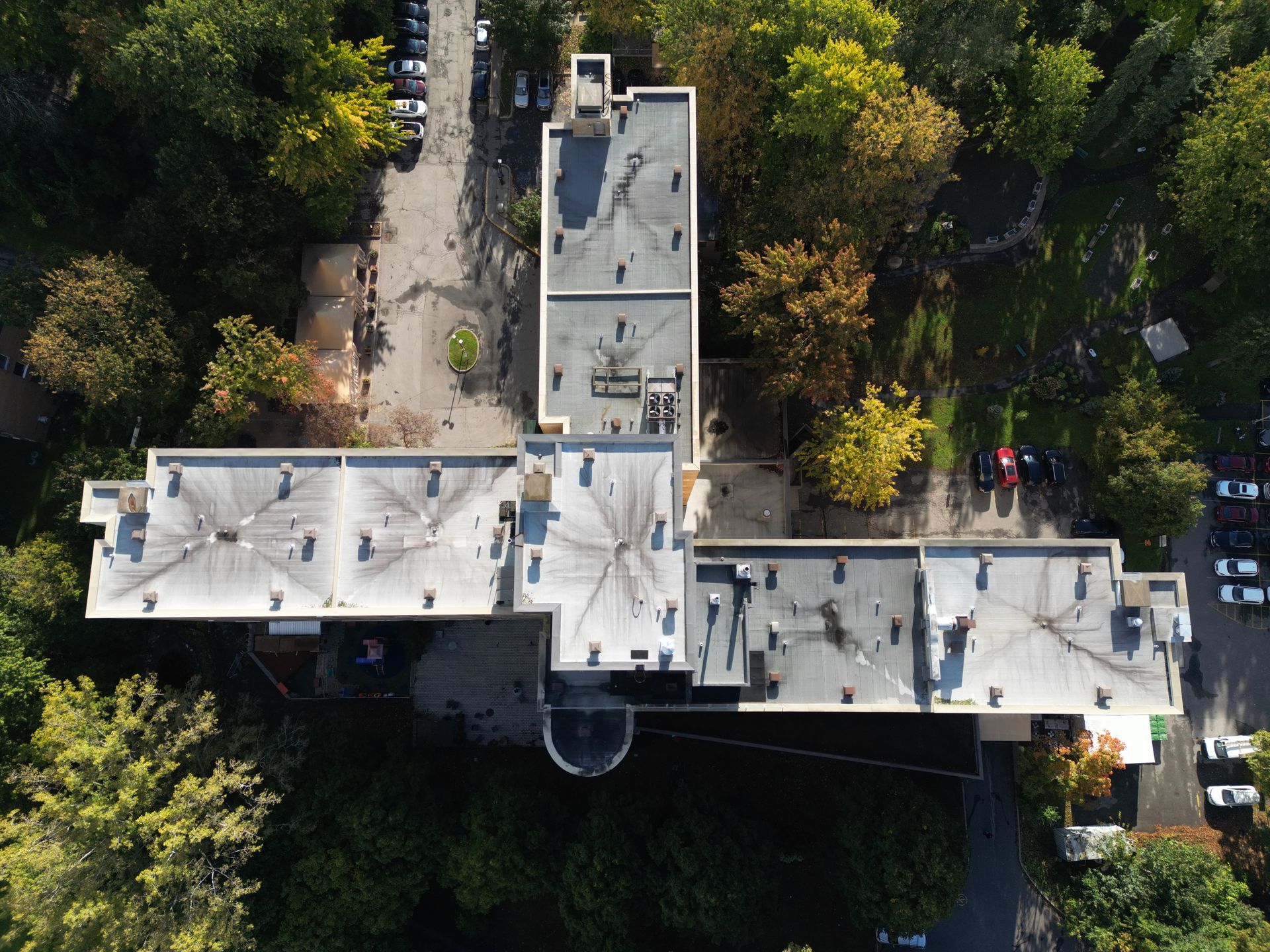 Aerial view of a white-roofed building surrounded by trees and a few parked cars