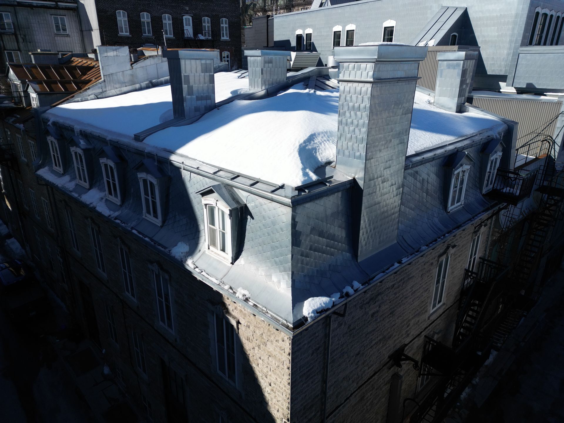 Snow-covered rooftop with chimneys on a brick building in an urban neighborhood
