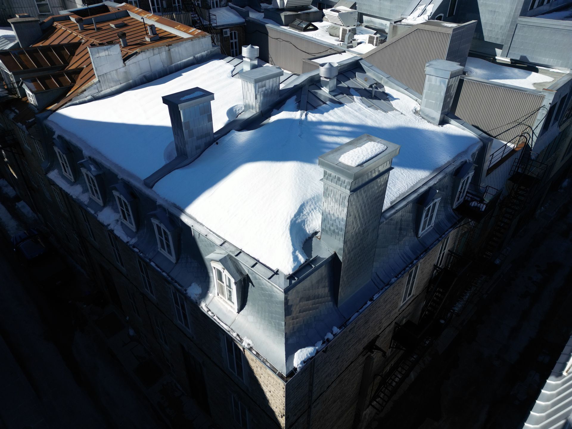 Snow-covered rooftops of a city building, viewed from above on a sunny winter day