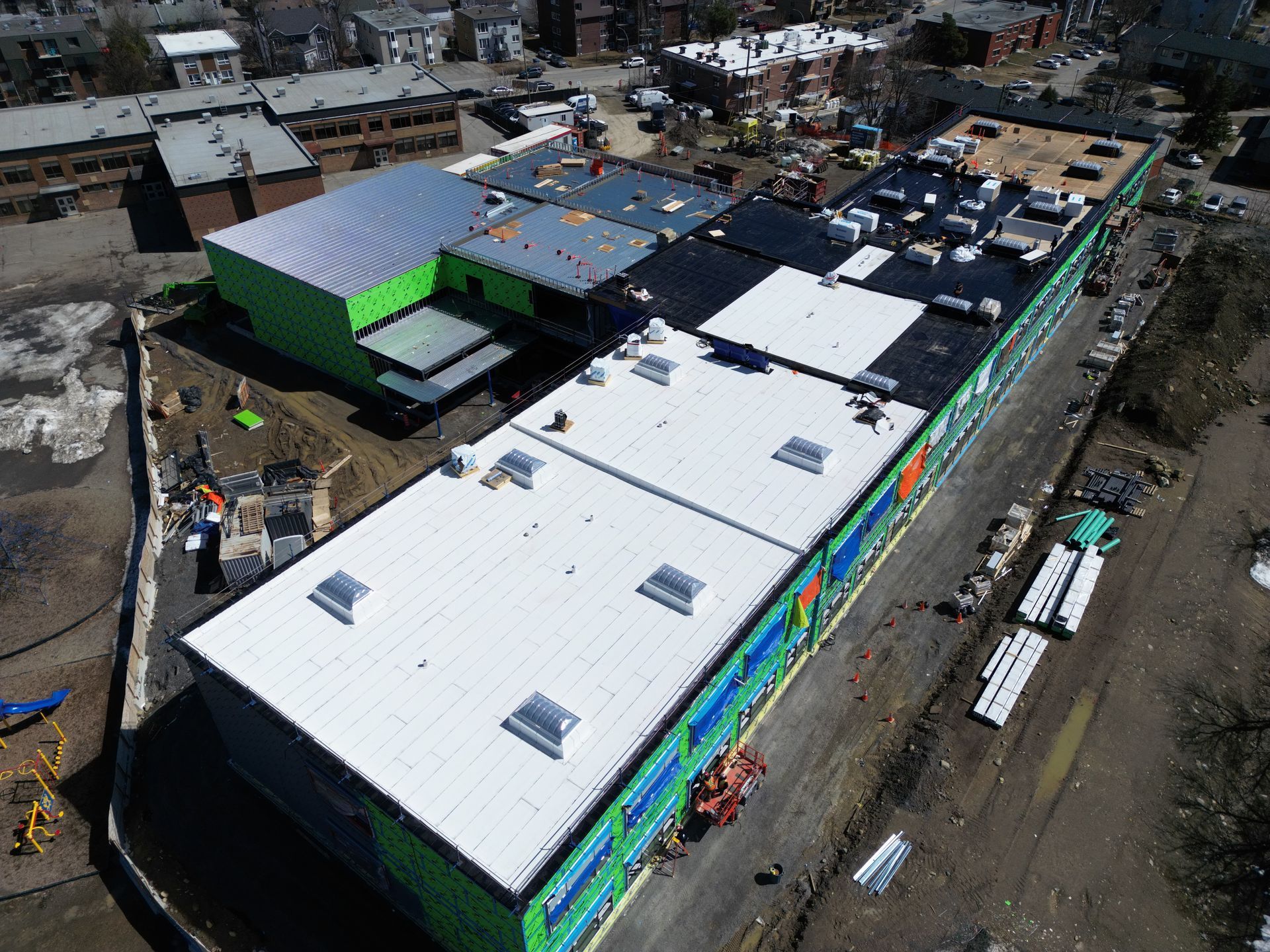 Aerial view of a large white-roofed building with colorful murals, surrounded by construction equipment and dirt lots