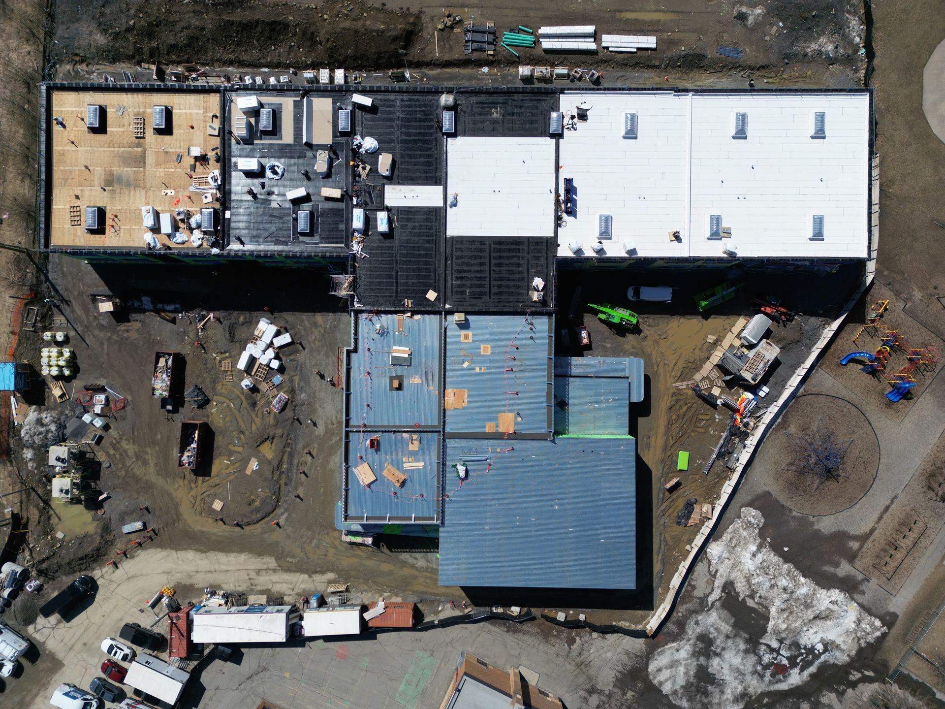 Aerial view of a construction site with buildings, trucks, dirt lots, and scattered equipment.