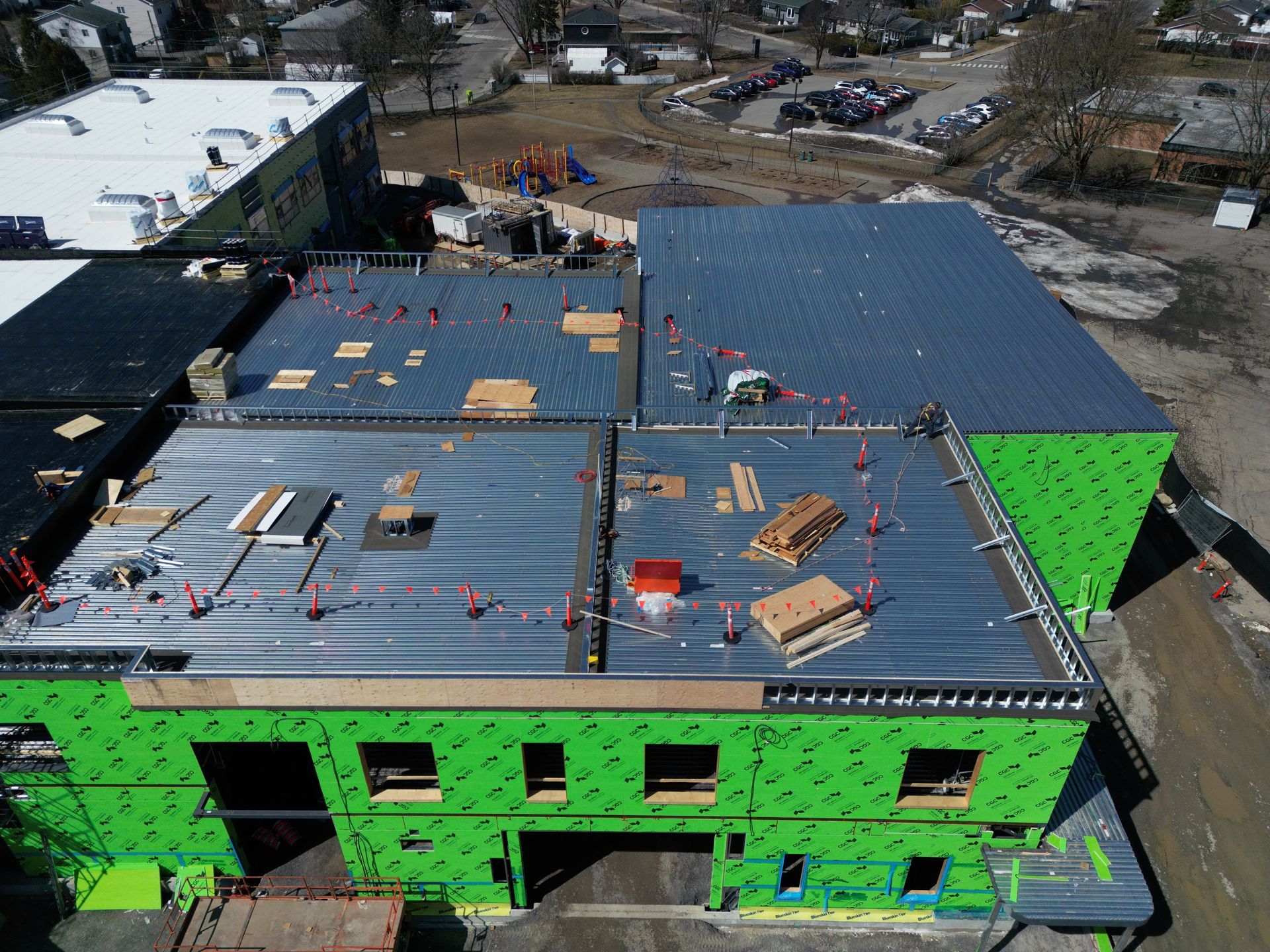 Aerial view of a building under construction with green exterior sheathing and a partially finished roof