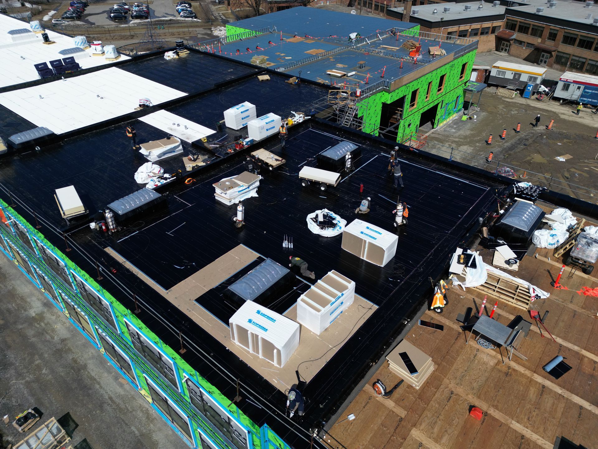 Aerial view of a building under construction with black roofing, white equipment, and green exterior framing.
