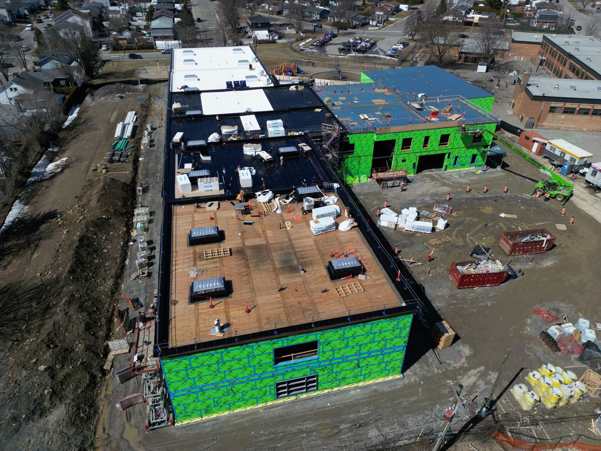 Aerial view of a damaged building with exposed roof and green tarp-covered walls amid flood debris.