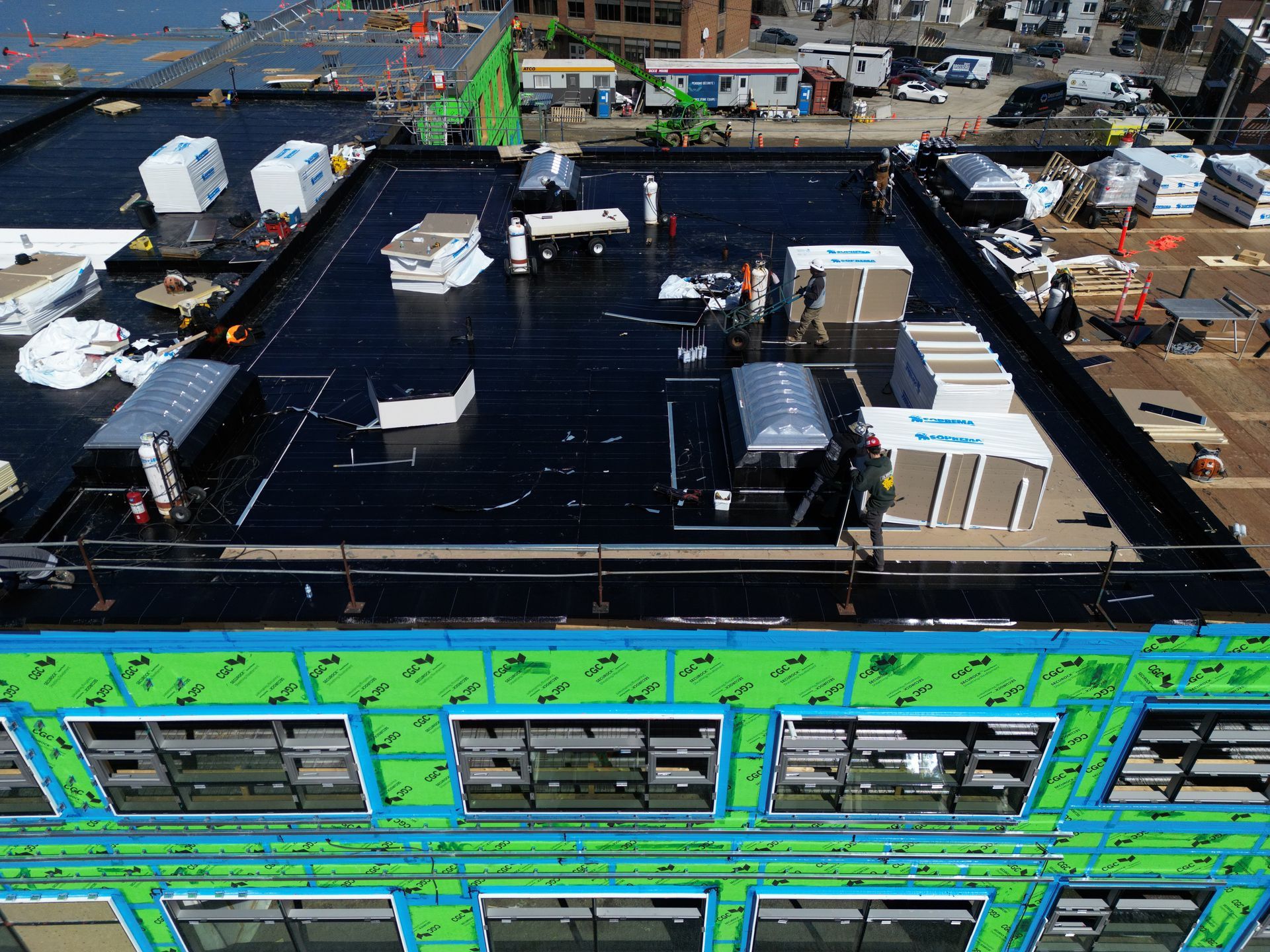Aerial view of a building under construction with a black roof, green facade panels, and industrial equipment nearby