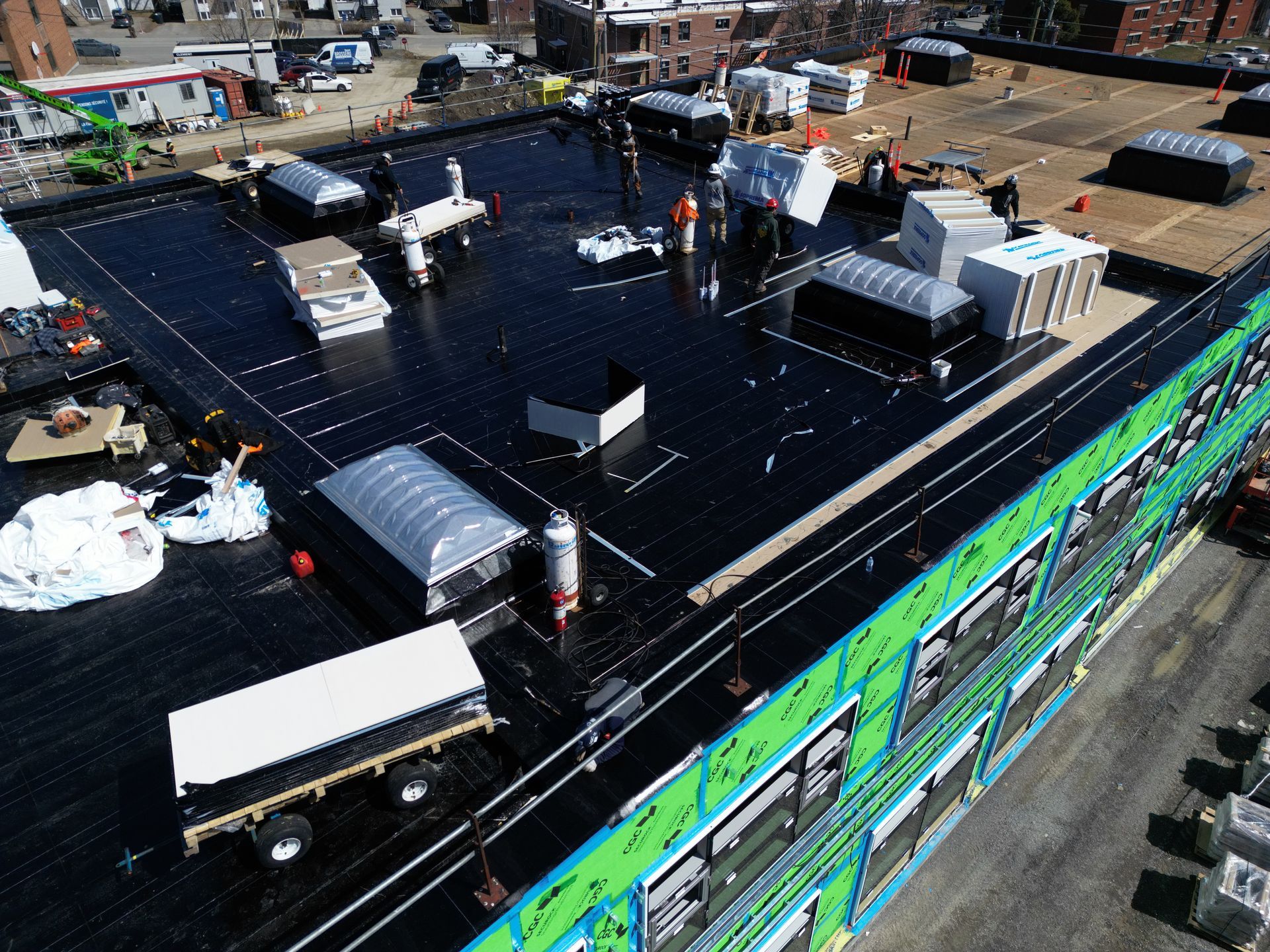 Rooftop with solar panels and HVAC units on a flat black roof beside colorful brick buildings.