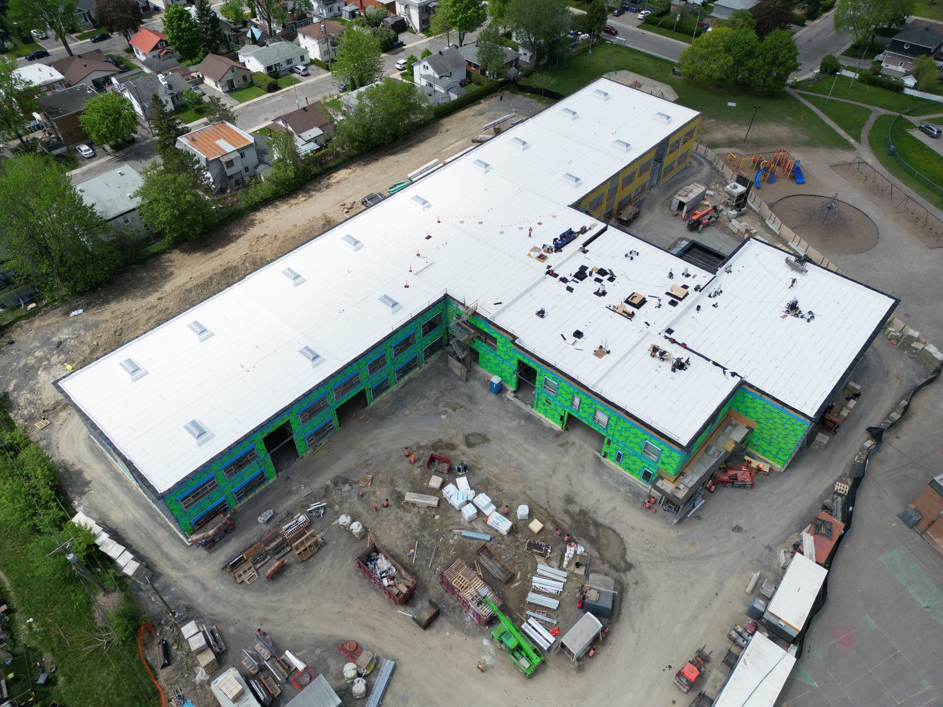 Aerial view of a large building under construction with a white roof and green exterior panels.