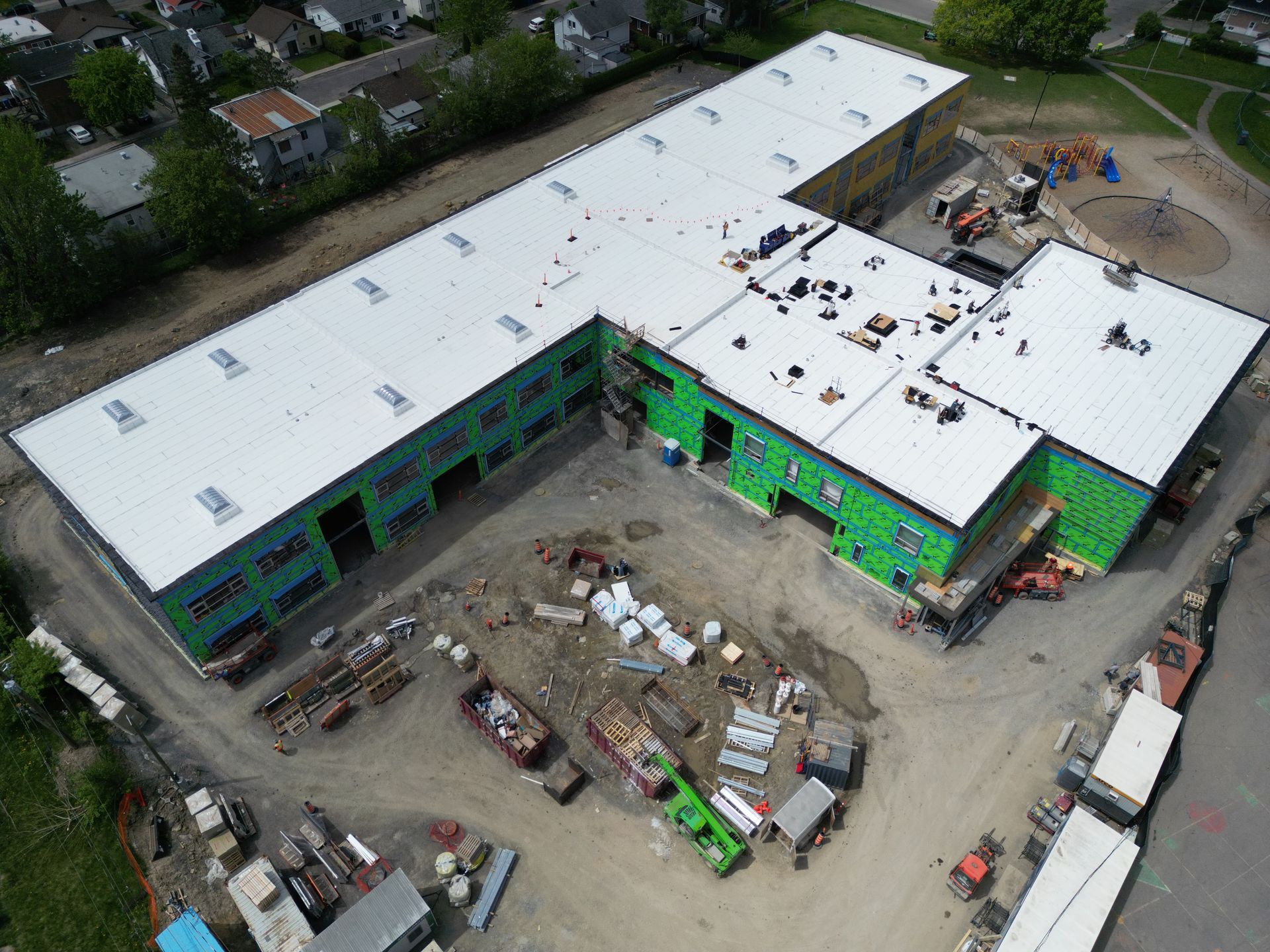 Aerial view of a large building under construction with a white roof and green exterior panels.