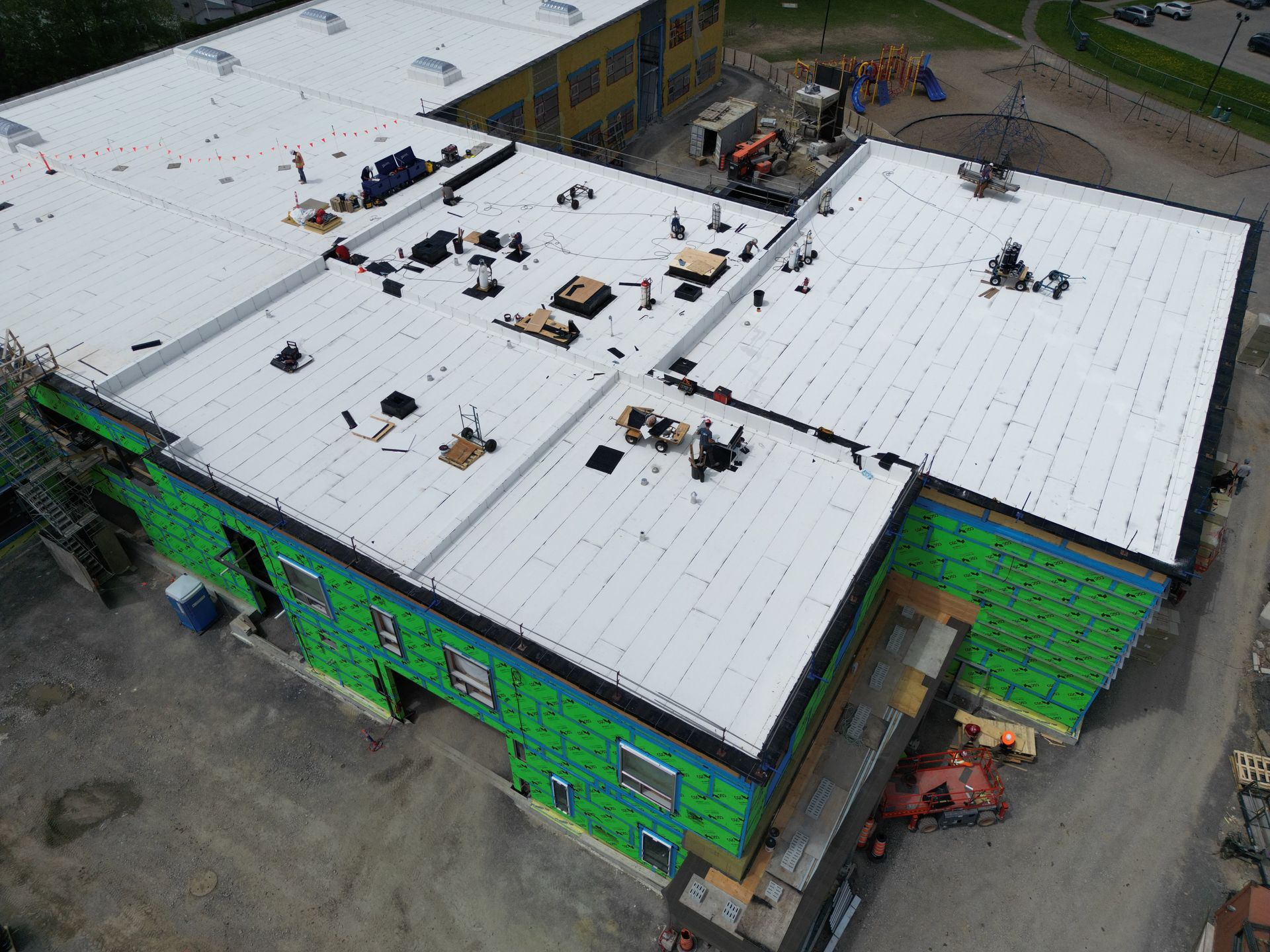 Aerial view of a green building with a white roof under construction, with materials and workers on top