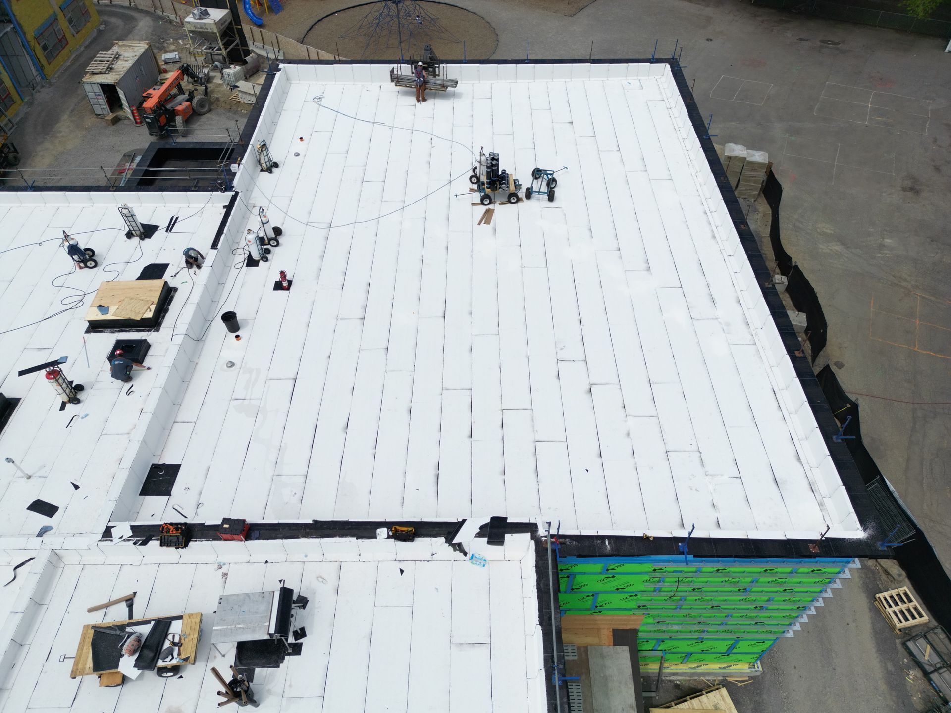 Aerial view of a large white roof under construction, with workers and equipment along the edges.