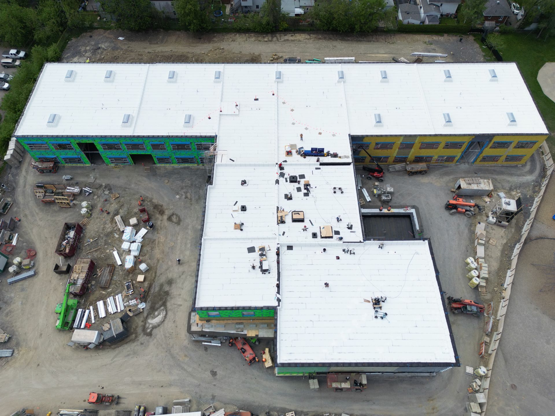 Aerial view of a large white-roofed building under construction with workers and equipment in the yard.