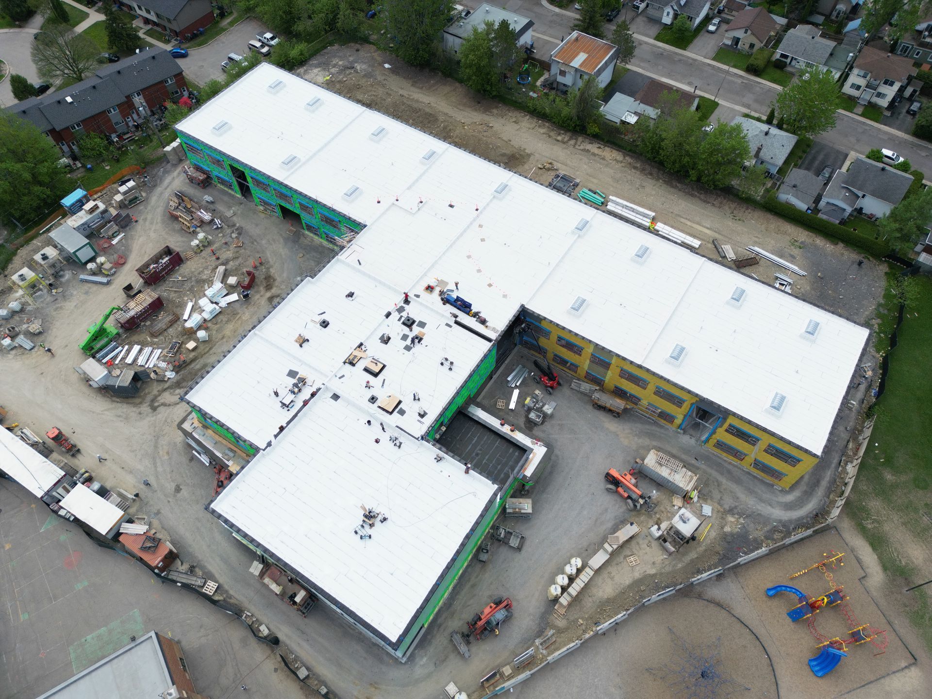 Aerial view of a school building with a white roof and construction equipment around it
