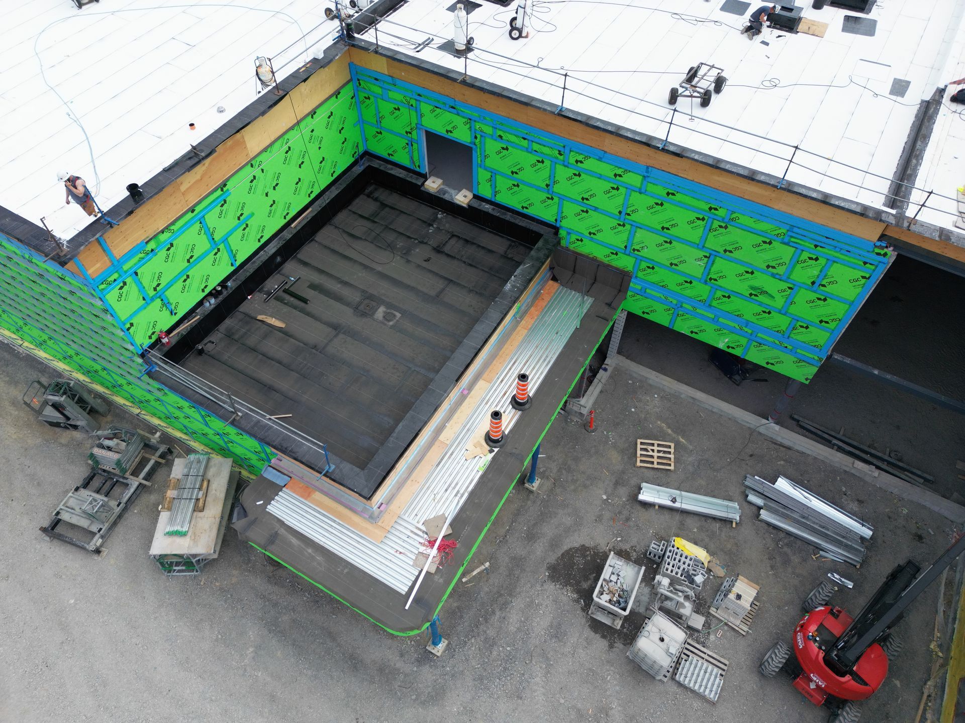 Aerial view of a construction site with green wall panels, rooftop work area, and scattered equipment.