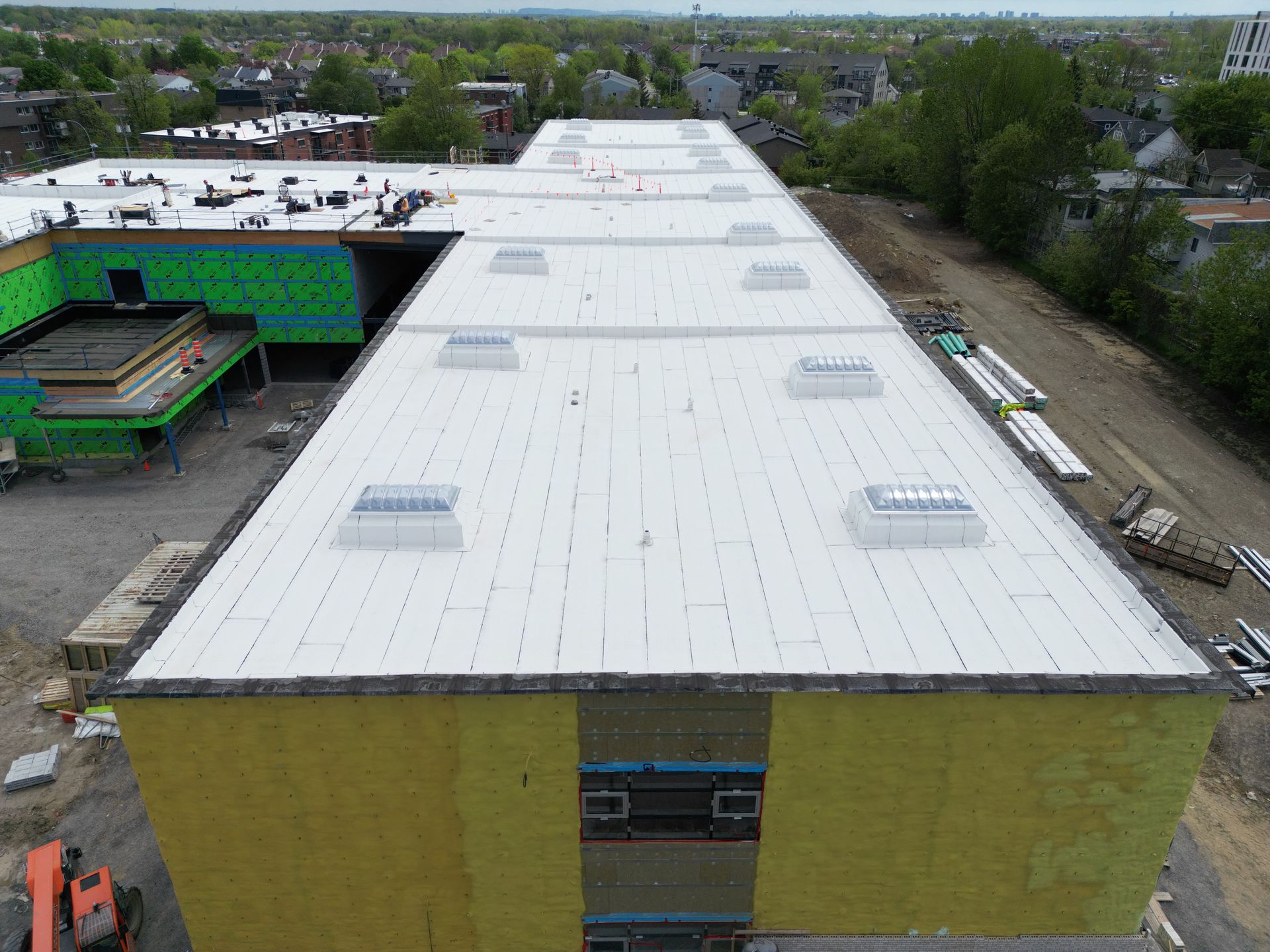 Aerial view of a large flat-roofed building under construction with white roofing and yellow walls.