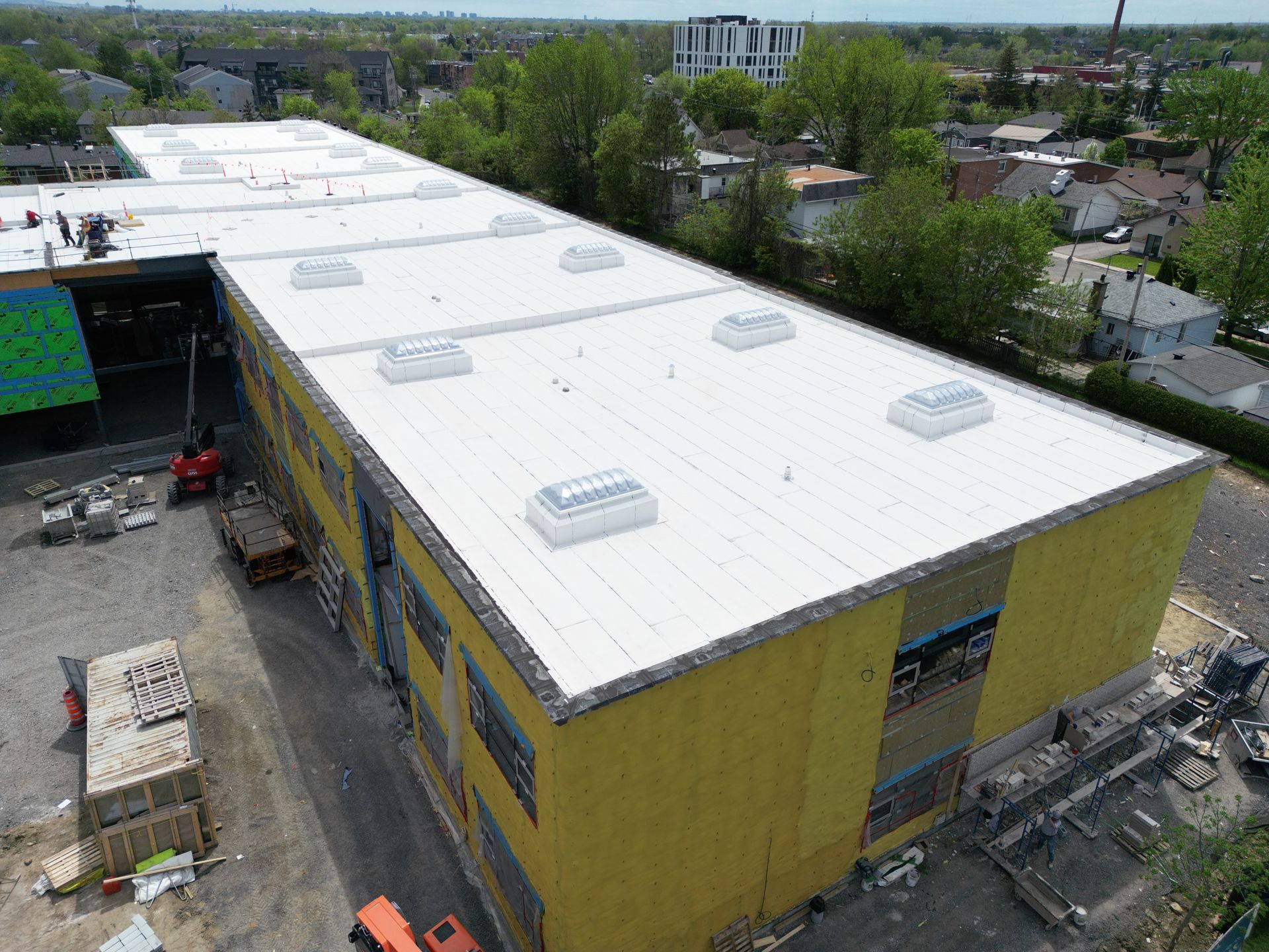 Aerial view of a large yellow building with a white roof and construction equipment nearby.