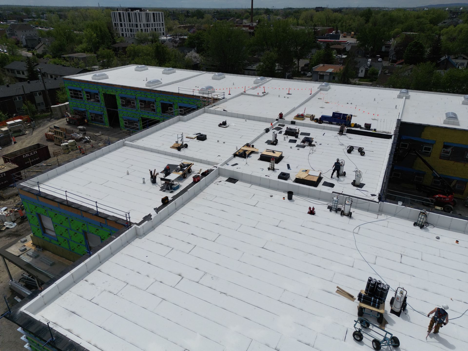 Aerial view of workers installing a white flat roof on a large building.