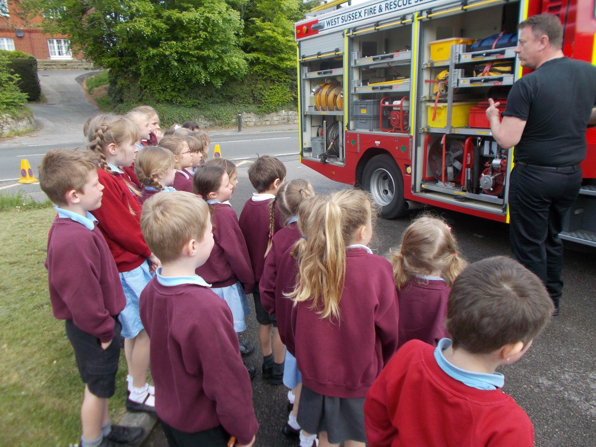 Children in school uniforms listen to a firefighter explaining equipment on a fire truck.