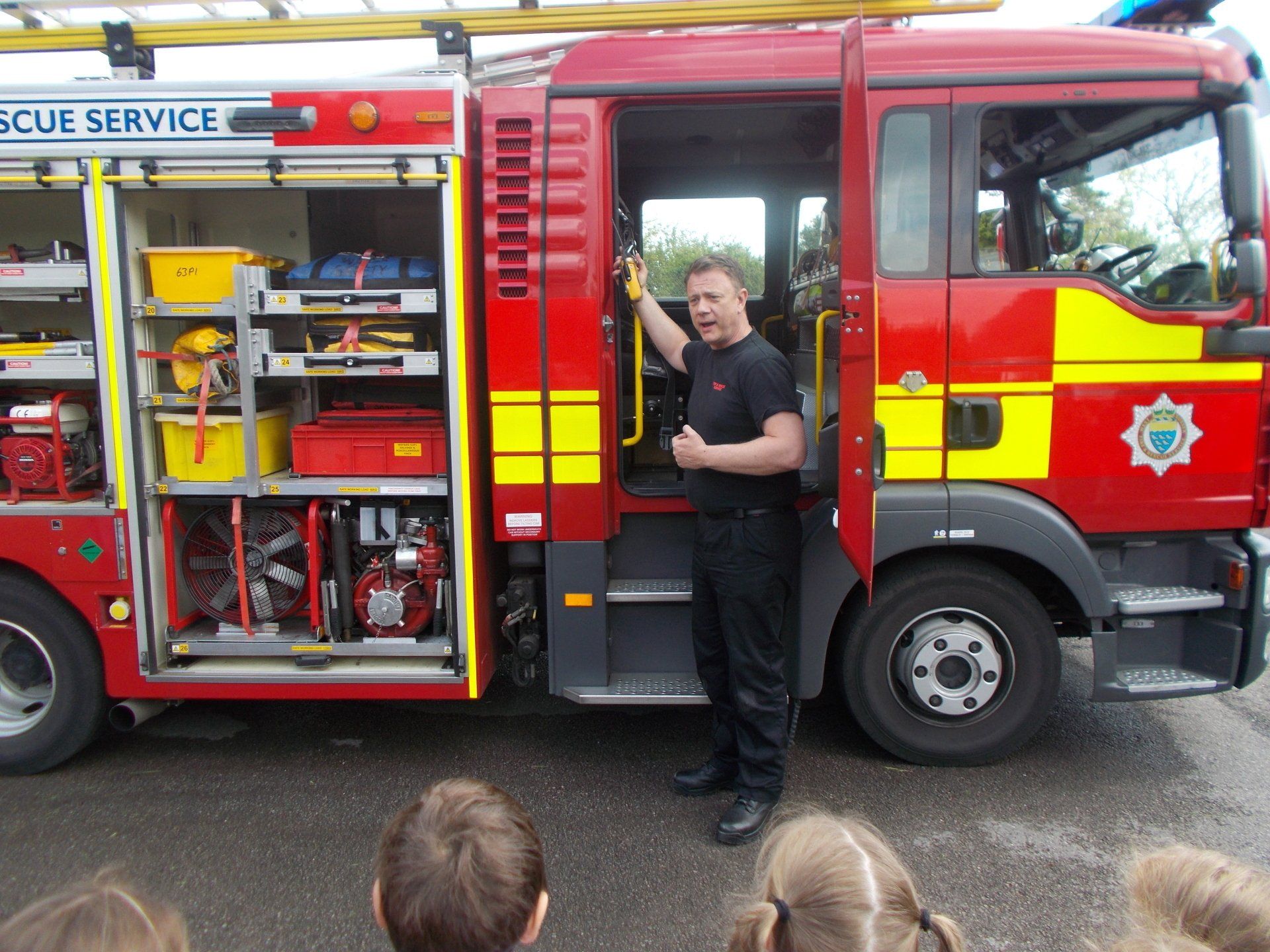 Firefighter showing equipment inside a red and yellow fire engine. Open door reveals tools.