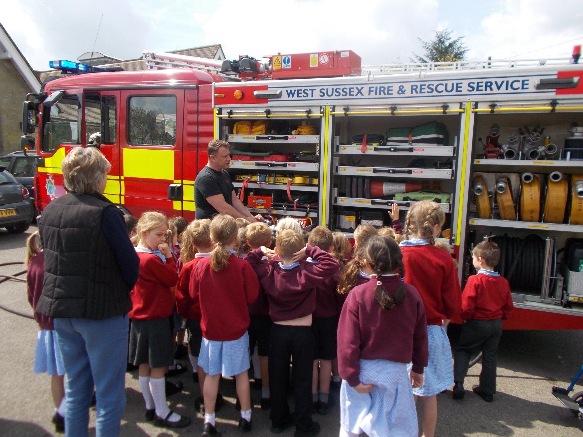 Firefighter showing equipment to a group of school children next to a red fire truck.