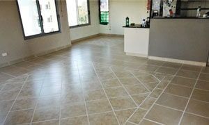 a living room with a tiled floor and a kitchen in the background .