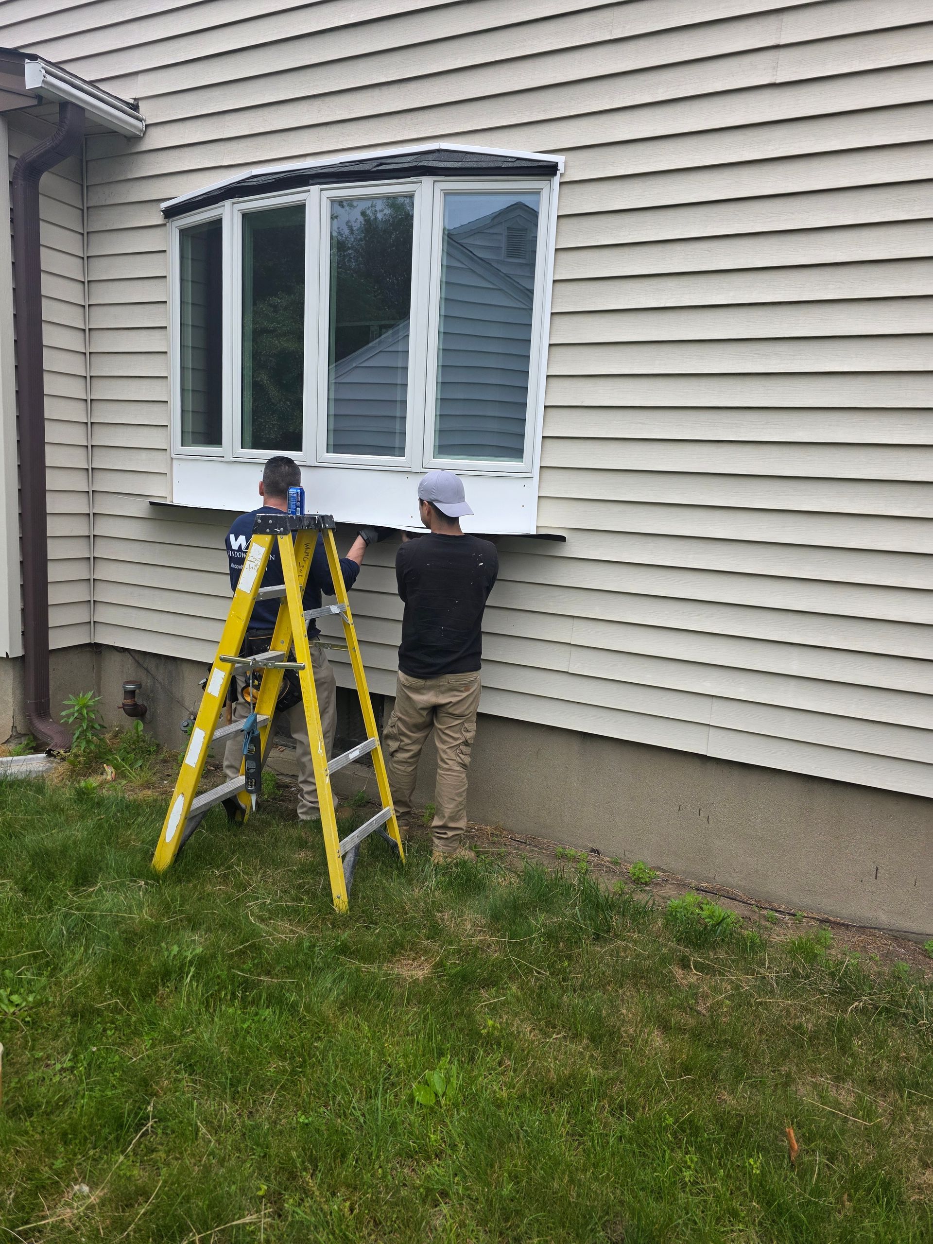 A man on a ladder is installing a window on the side of a house.