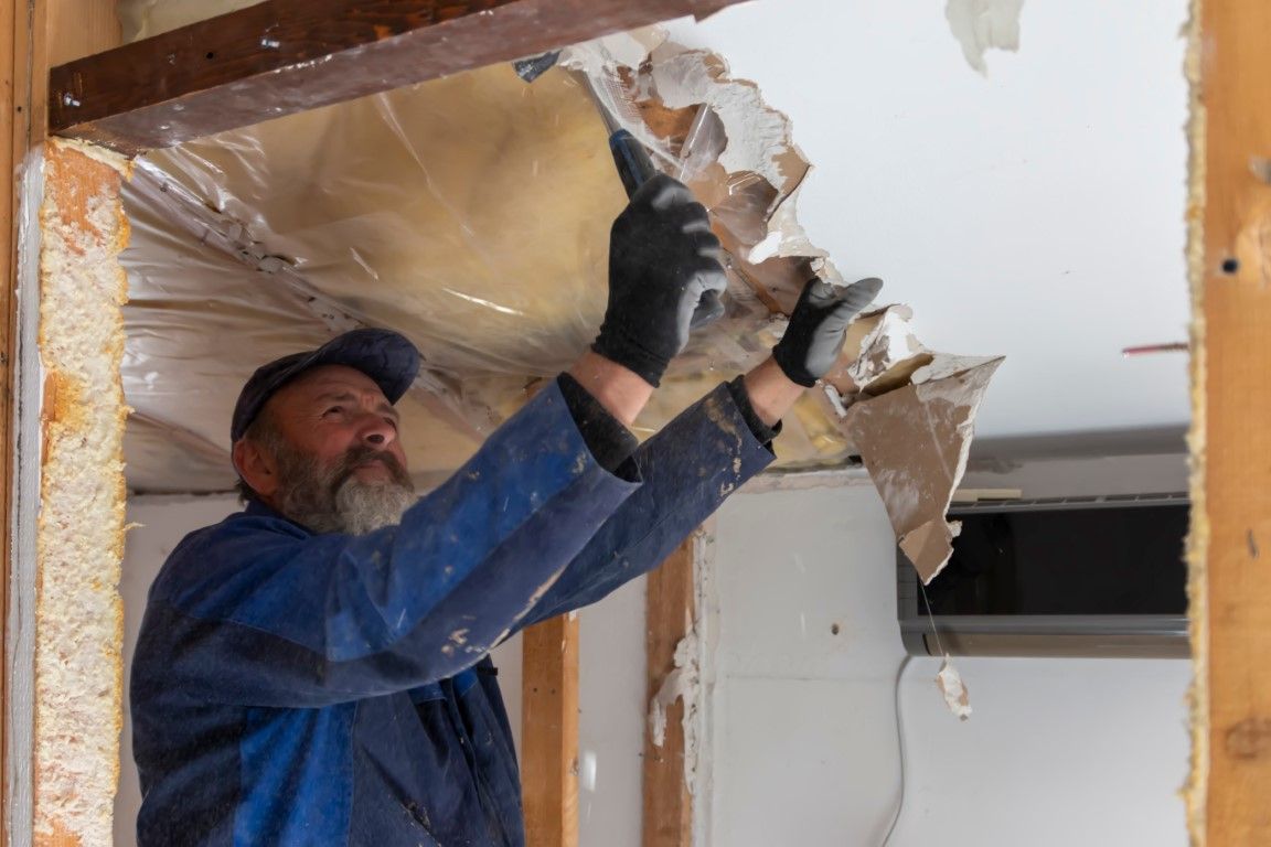 Worker tearing down drywall with a hammer in an unfinished room