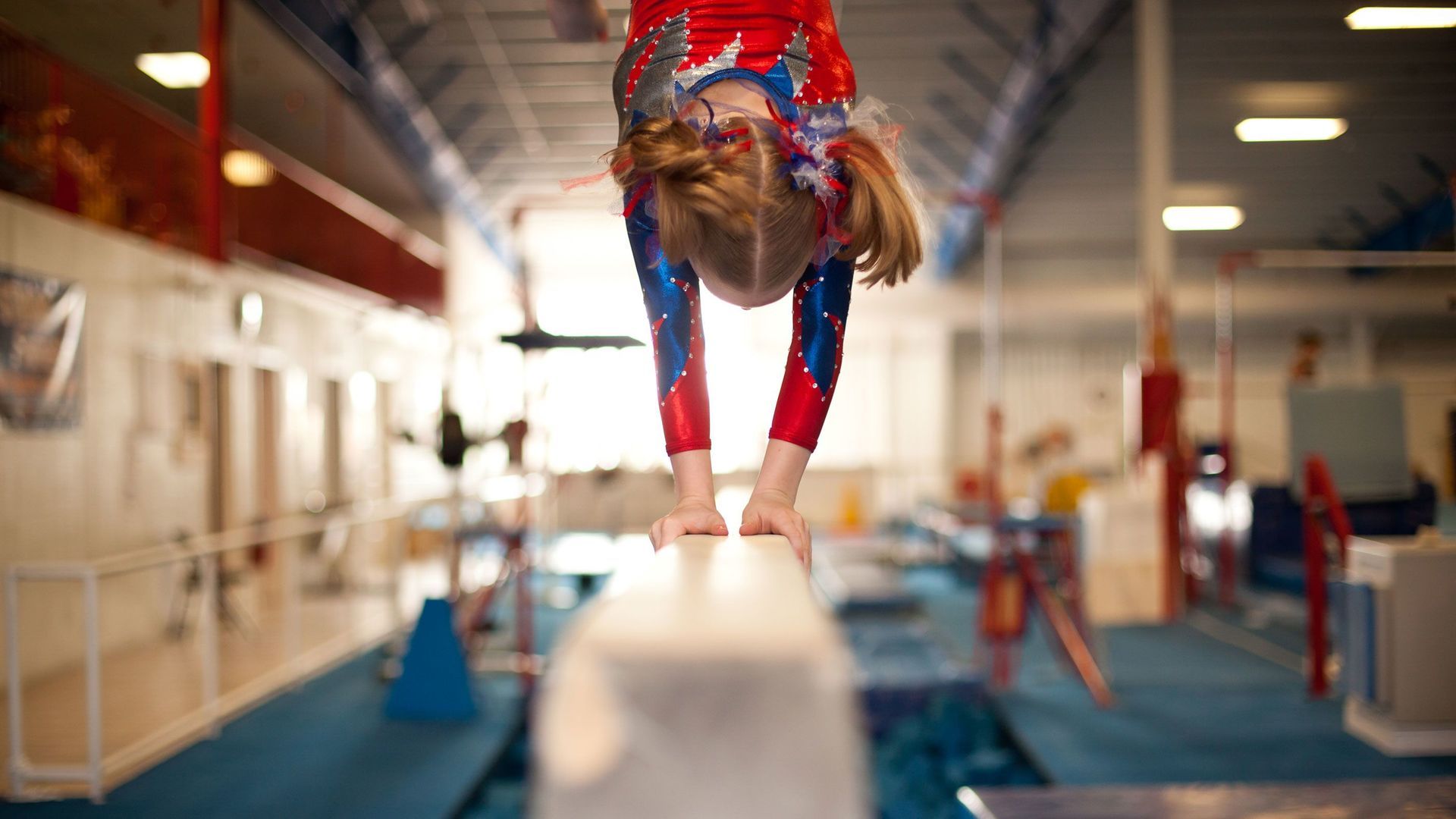 A young girl is doing a handstand on a balance beam in a gym.
