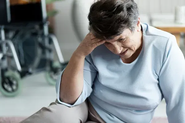 An elderly woman is sitting on the floor with her head in her hand.
