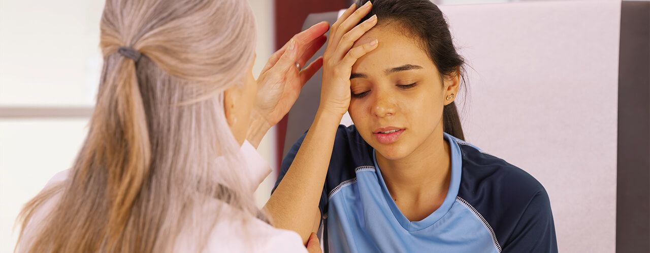 A woman is holding her head while talking to a doctor.
