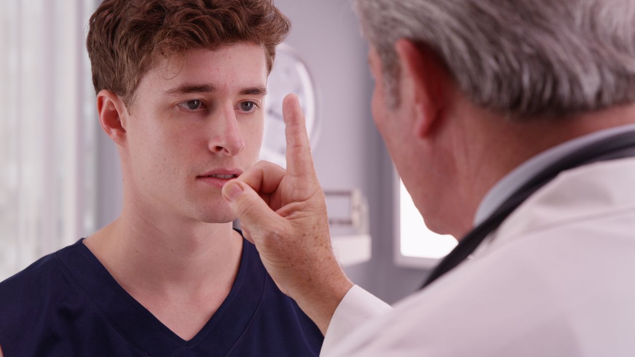 A doctor is examining a young man 's eye in a hospital.
