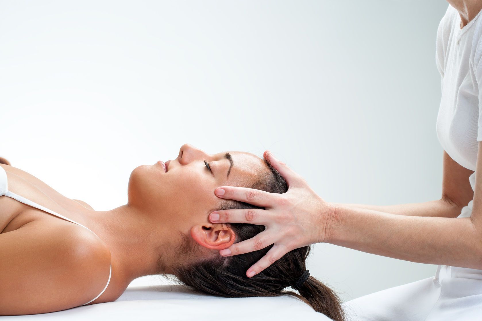 A woman is laying on a table getting a head massage.