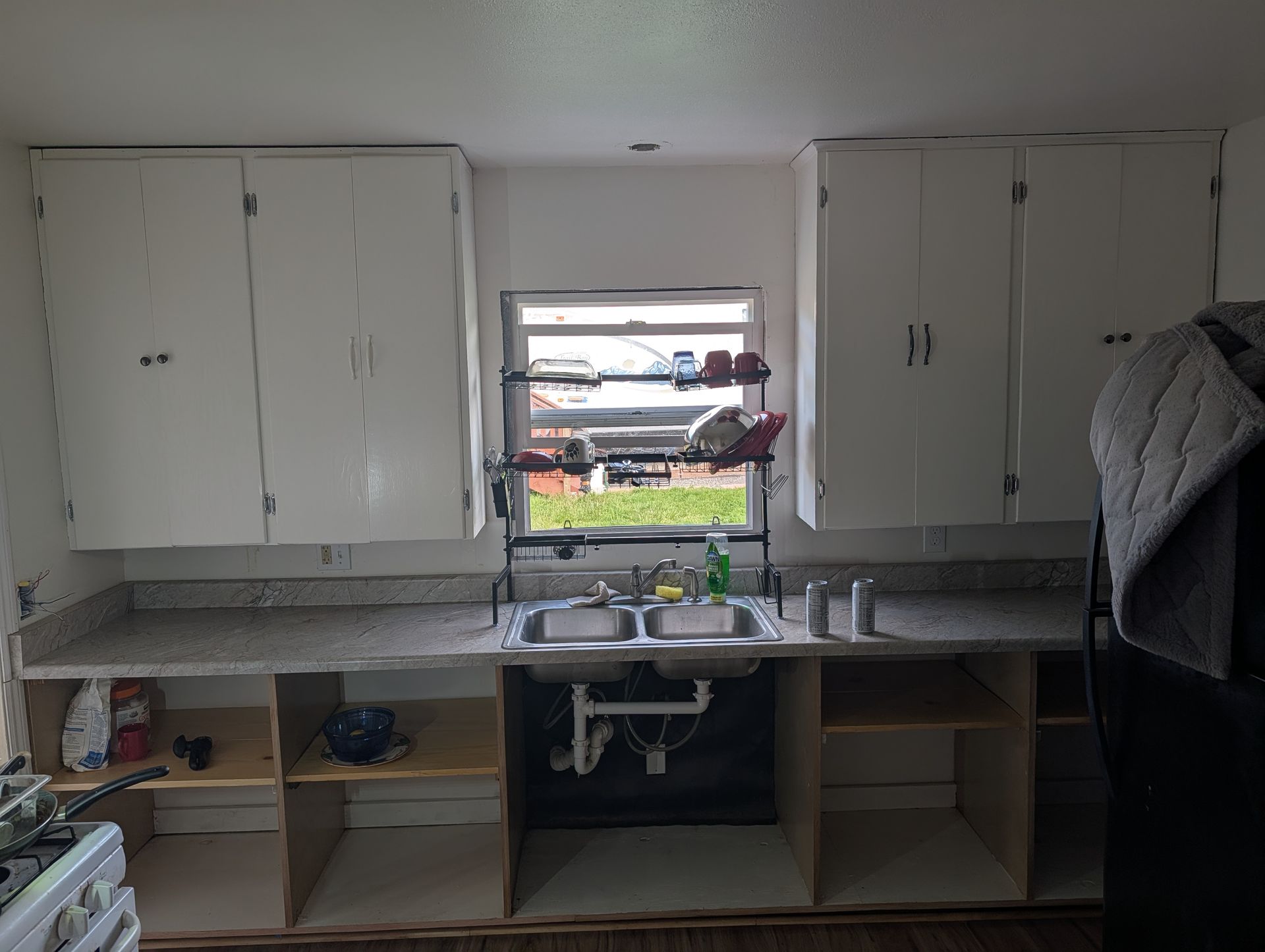 Kitchen sink under window with white cabinets and countertop, seen from inside a room