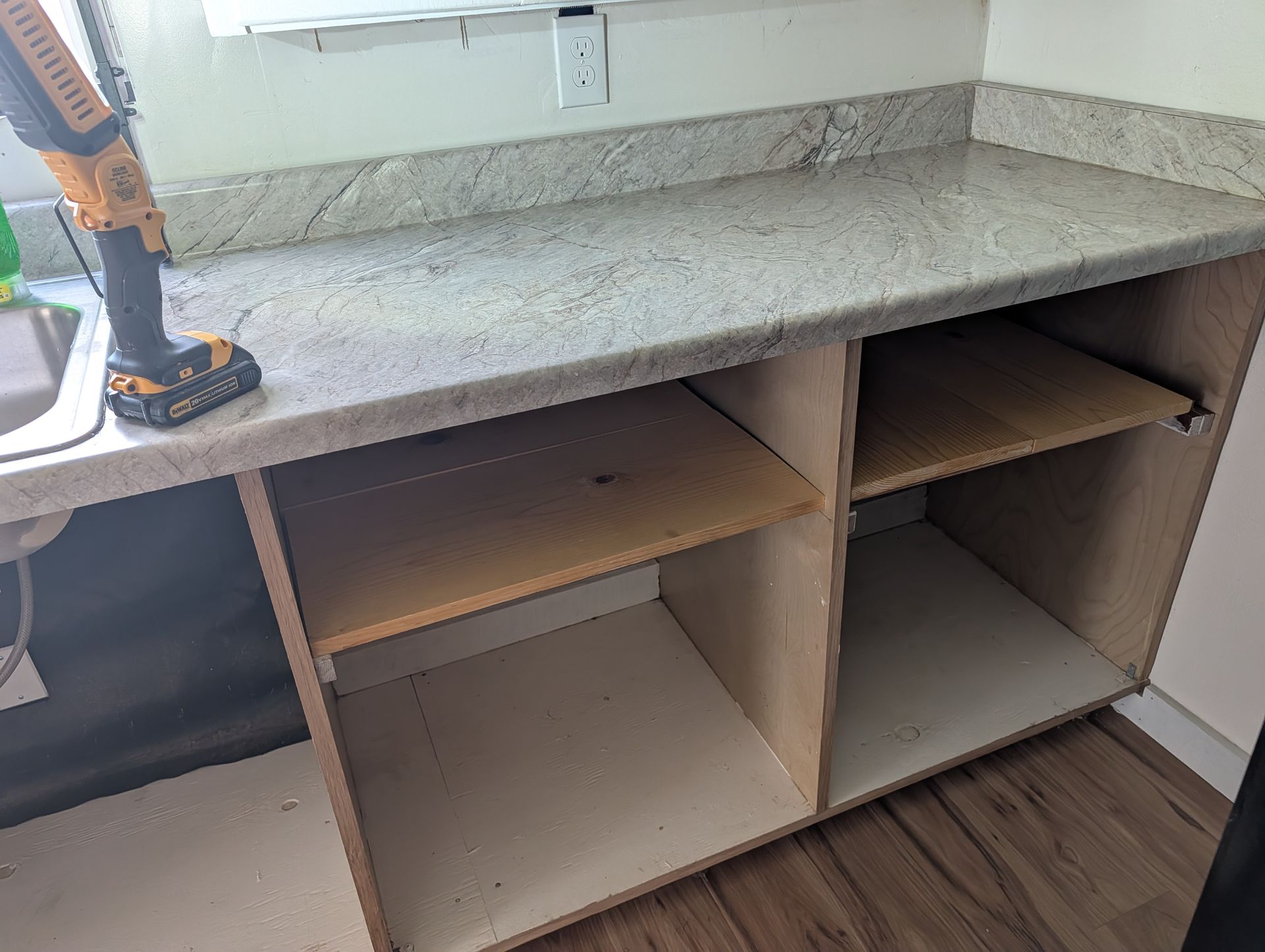 Empty kitchen cabinet under a speckled countertop with unfinished shelves and open cubbies.
