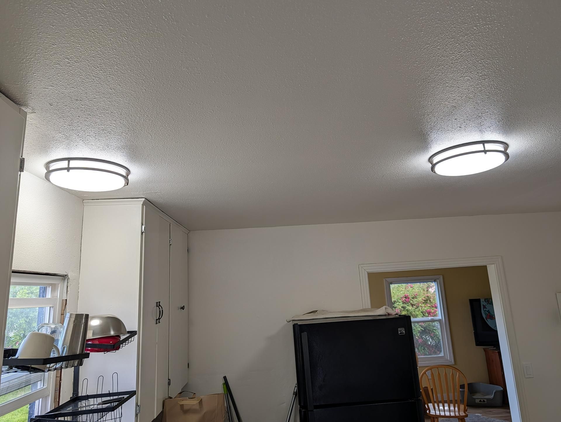 Small kitchen with white cabinets, two ceiling lights, and a black cabinet near a doorway.