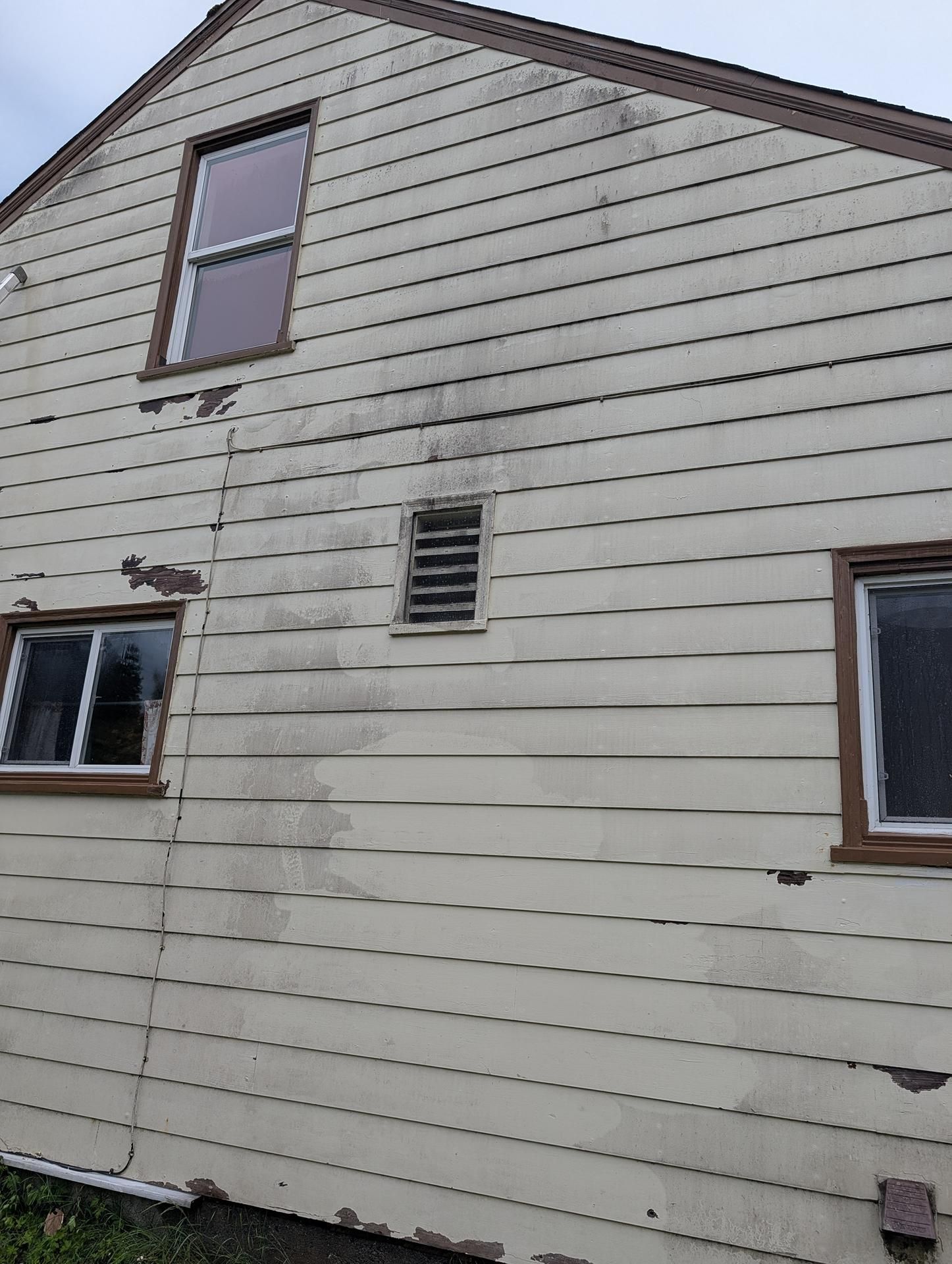Side of a beige house with horizontal siding, two windows, and a small vent.