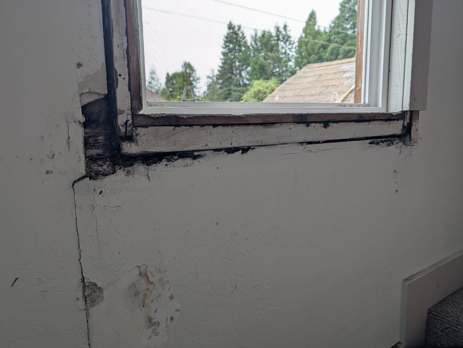 Old window with peeling paint and dark, damaged trim on an interior wall.