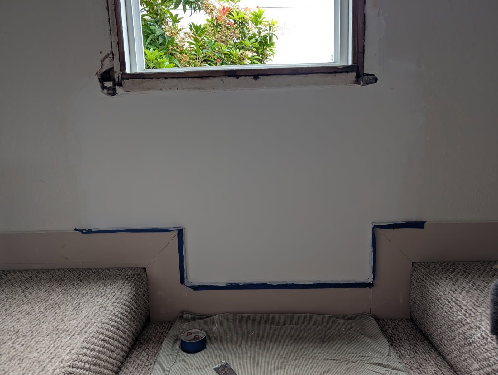 Small room with a window, two gray sofas, and blue tape marking a low wall outline.